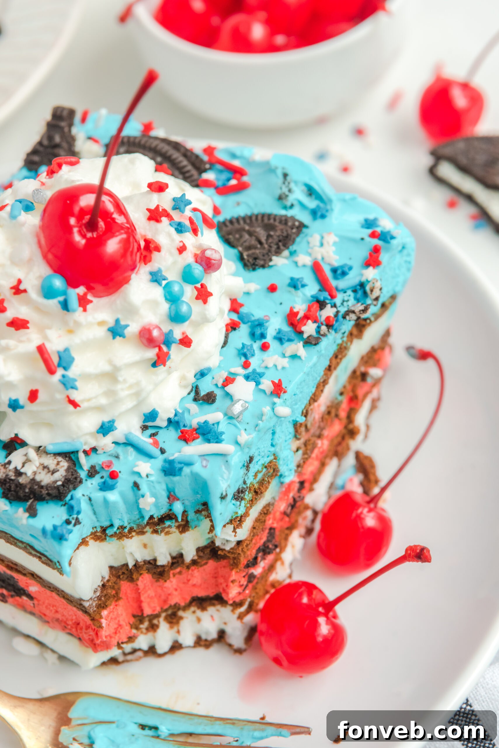 Close up view of a slice of Patriotic Ice Cream Sandwich Cake topped with whipped cream and cherry.