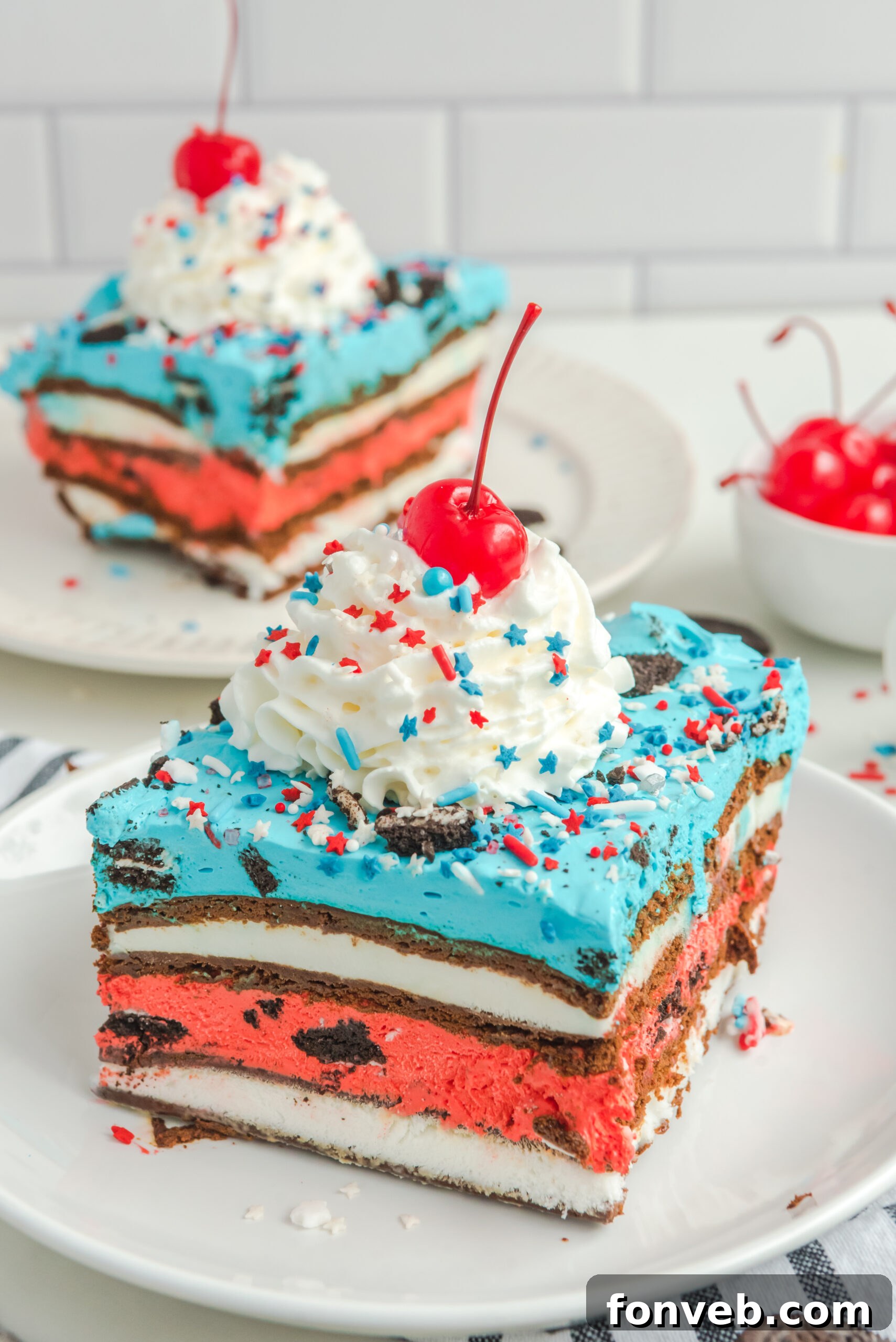 Front view of a slice of Patriotic Ice Cream Sandwich Cake topped with whipped cream and cherry.