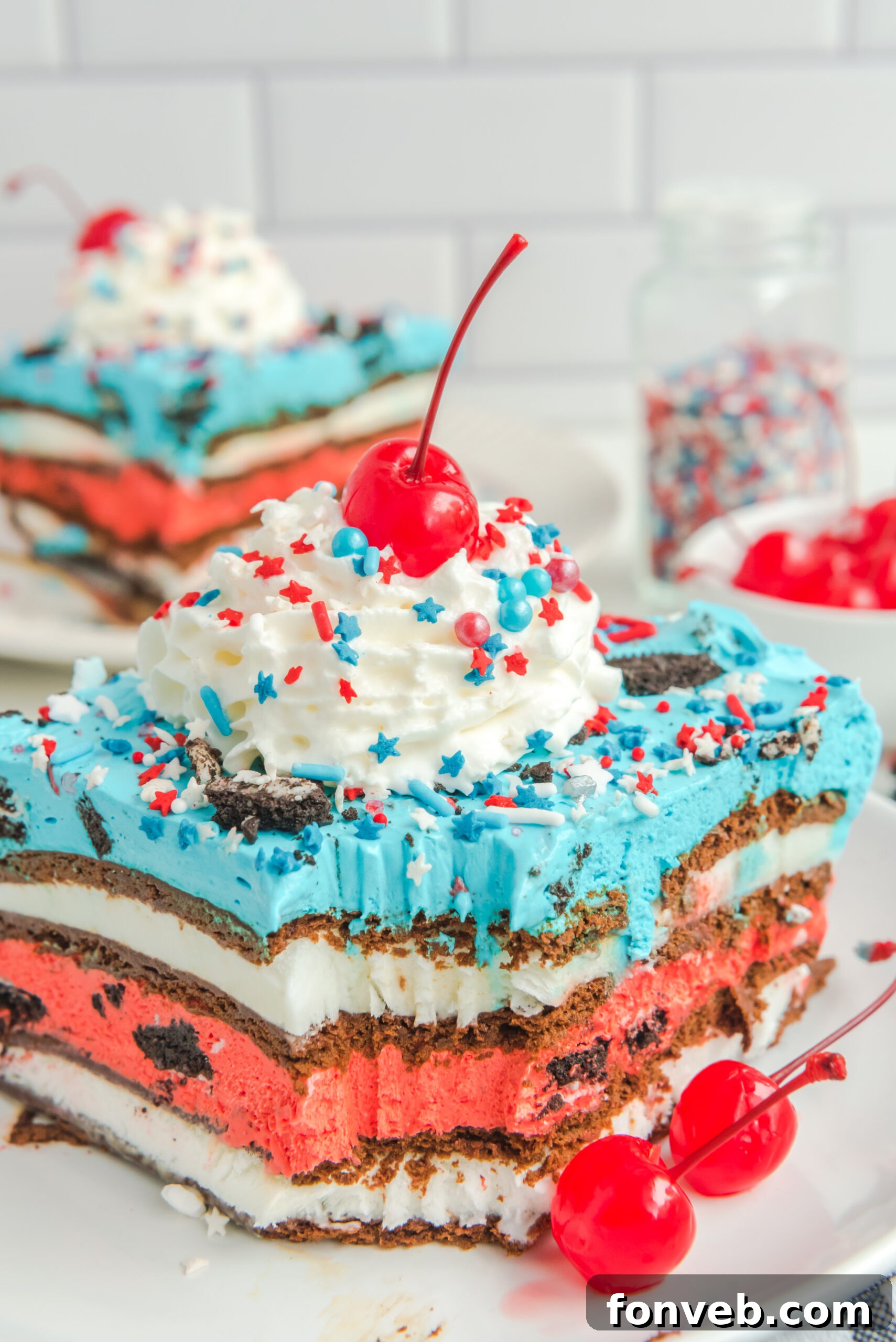 Front view of a slice of Patriotic Ice Cream Sandwich Cake with a bite missing topped with whipped cream and cherry.