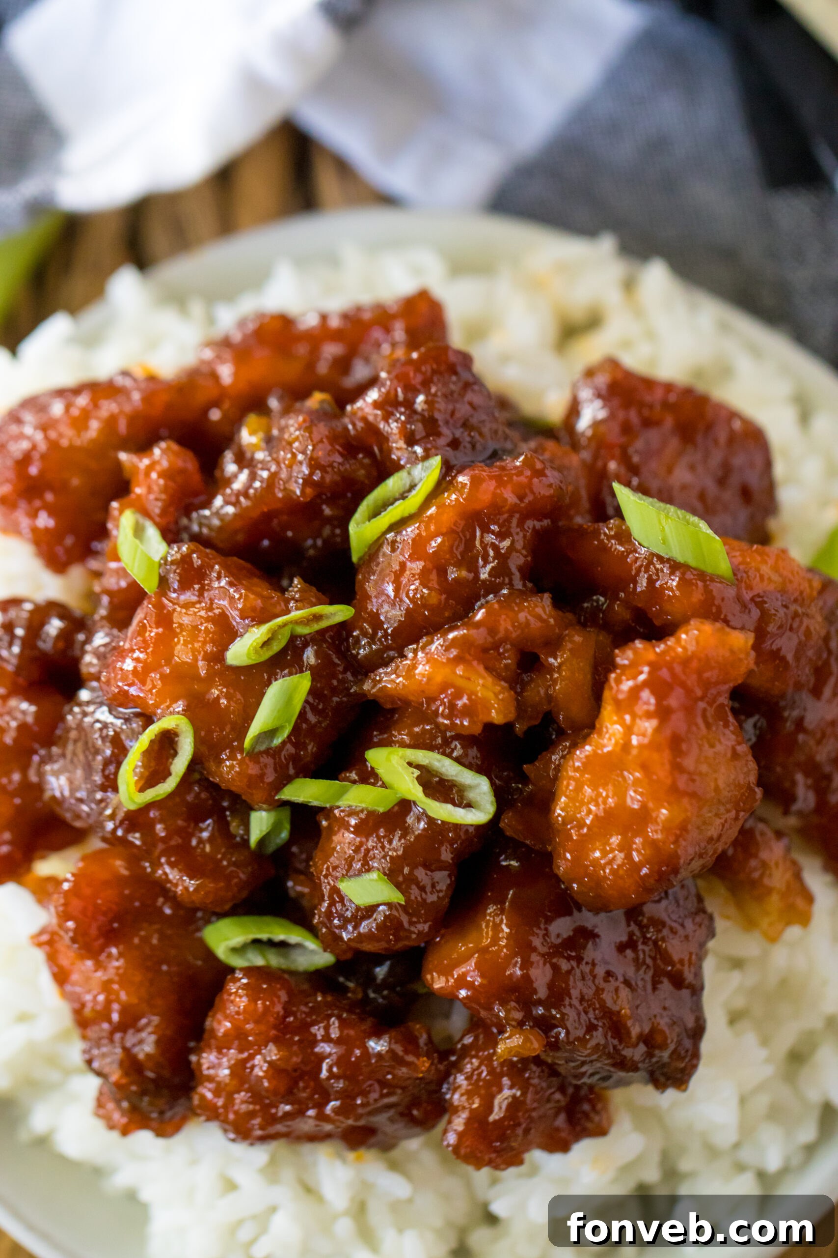 Overhead view of Slow Cooker Firecracker Chicken over white rice in a white bowl, garnished with fresh green onions.