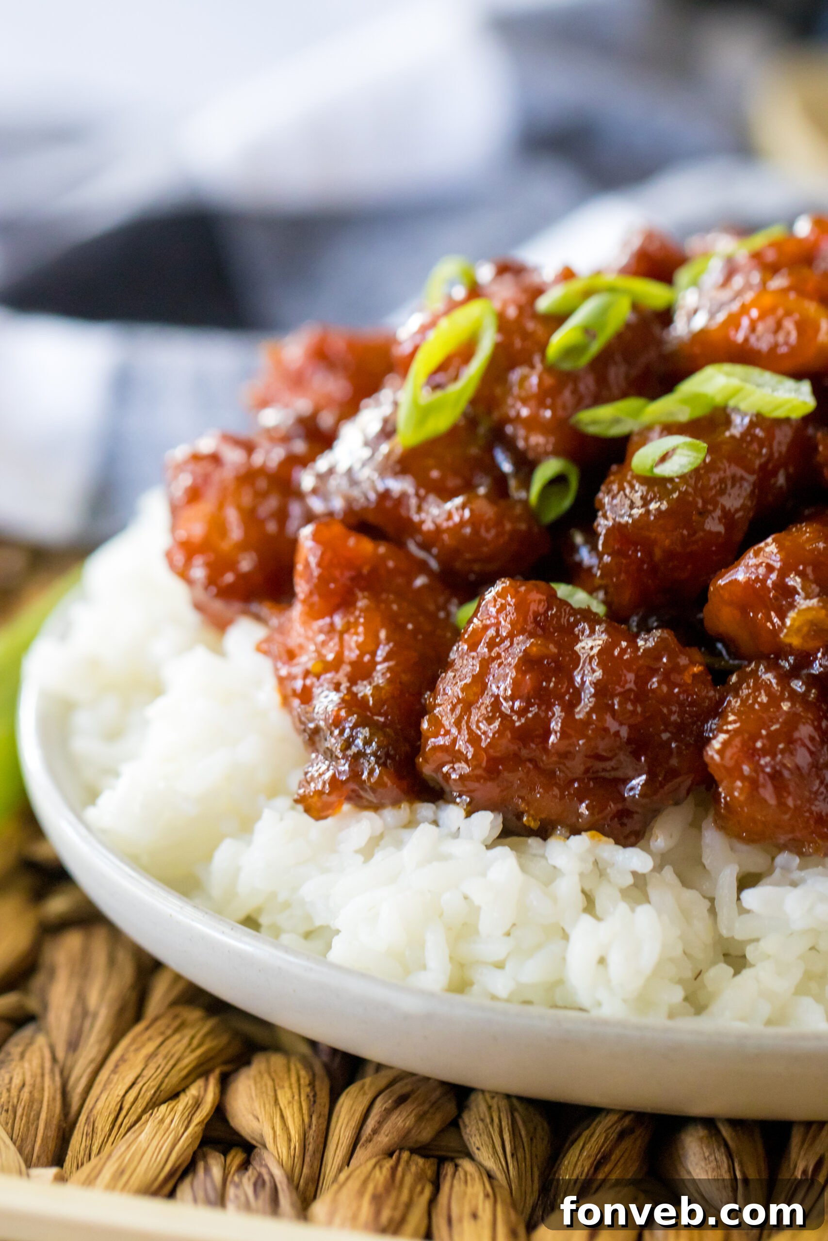 Close up view of Slow Cooker Firecracker Chicken over white rice in a white bowl, with a focus on the glossy sauce.