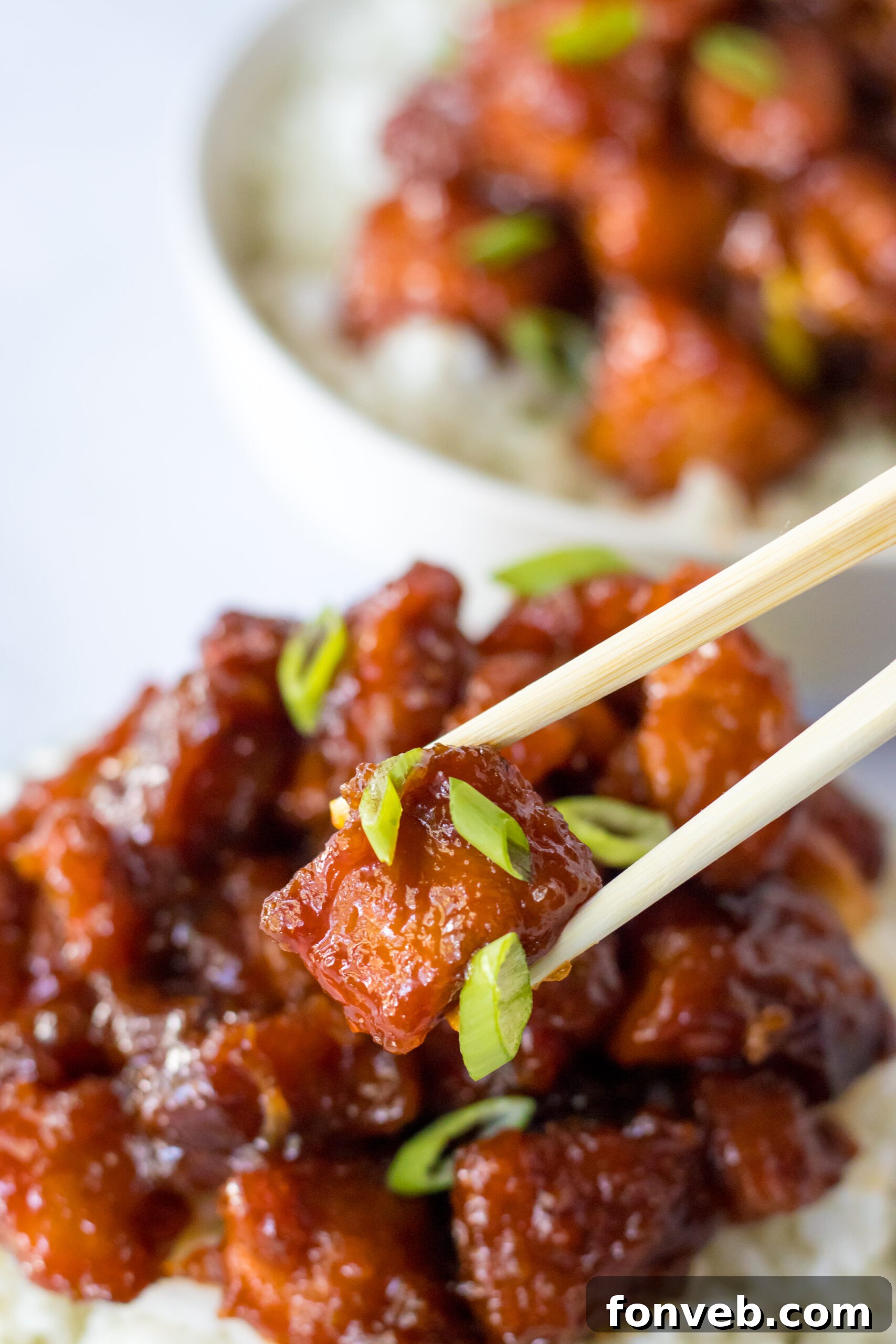 Close up view of chopsticks holding a perfectly glazed piece of Slow Cooker Firecracker Chicken.