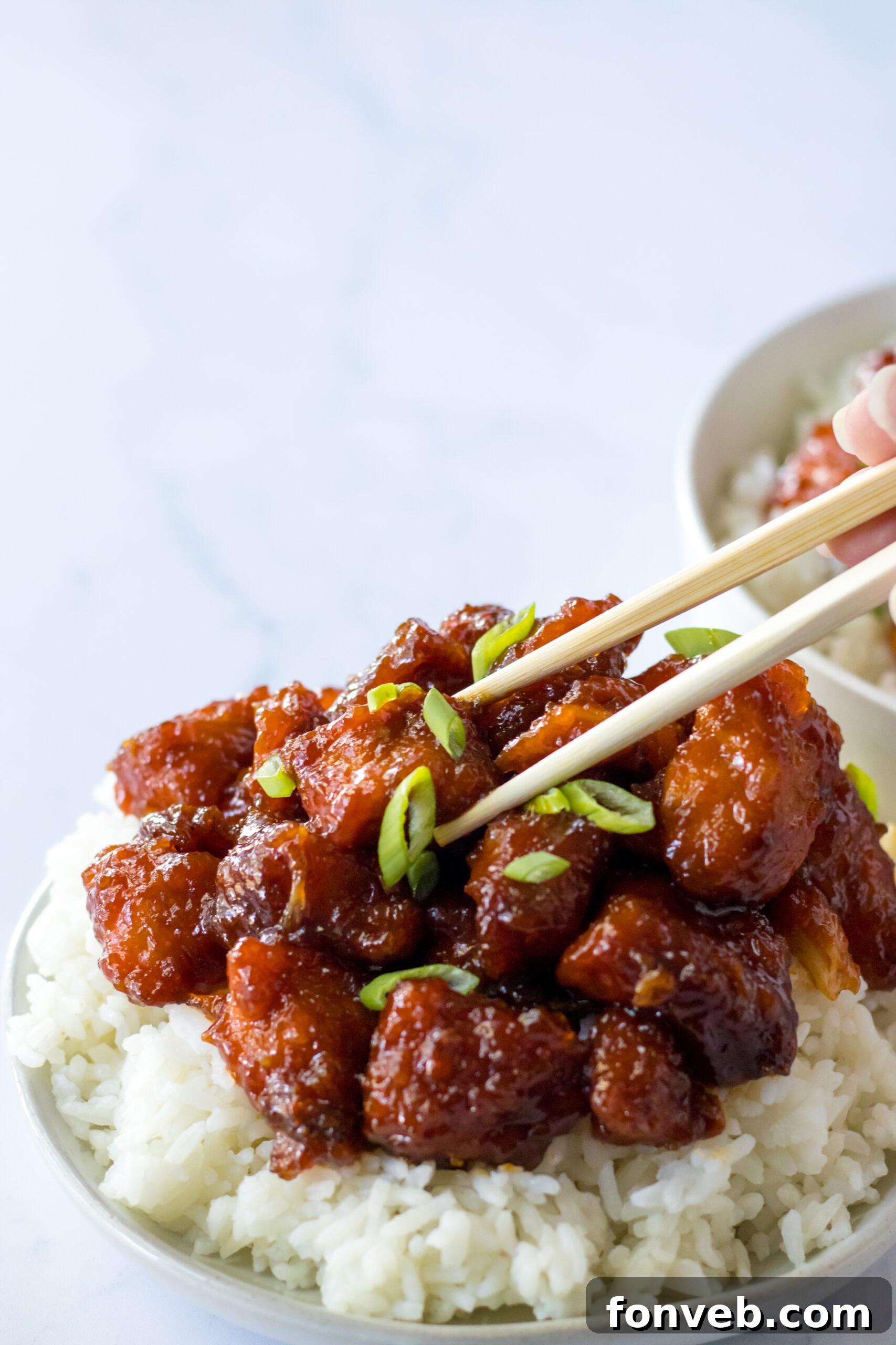 Close up view of chopsticks holding another piece of Slow Cooker Firecracker Chicken, emphasizing its texture.