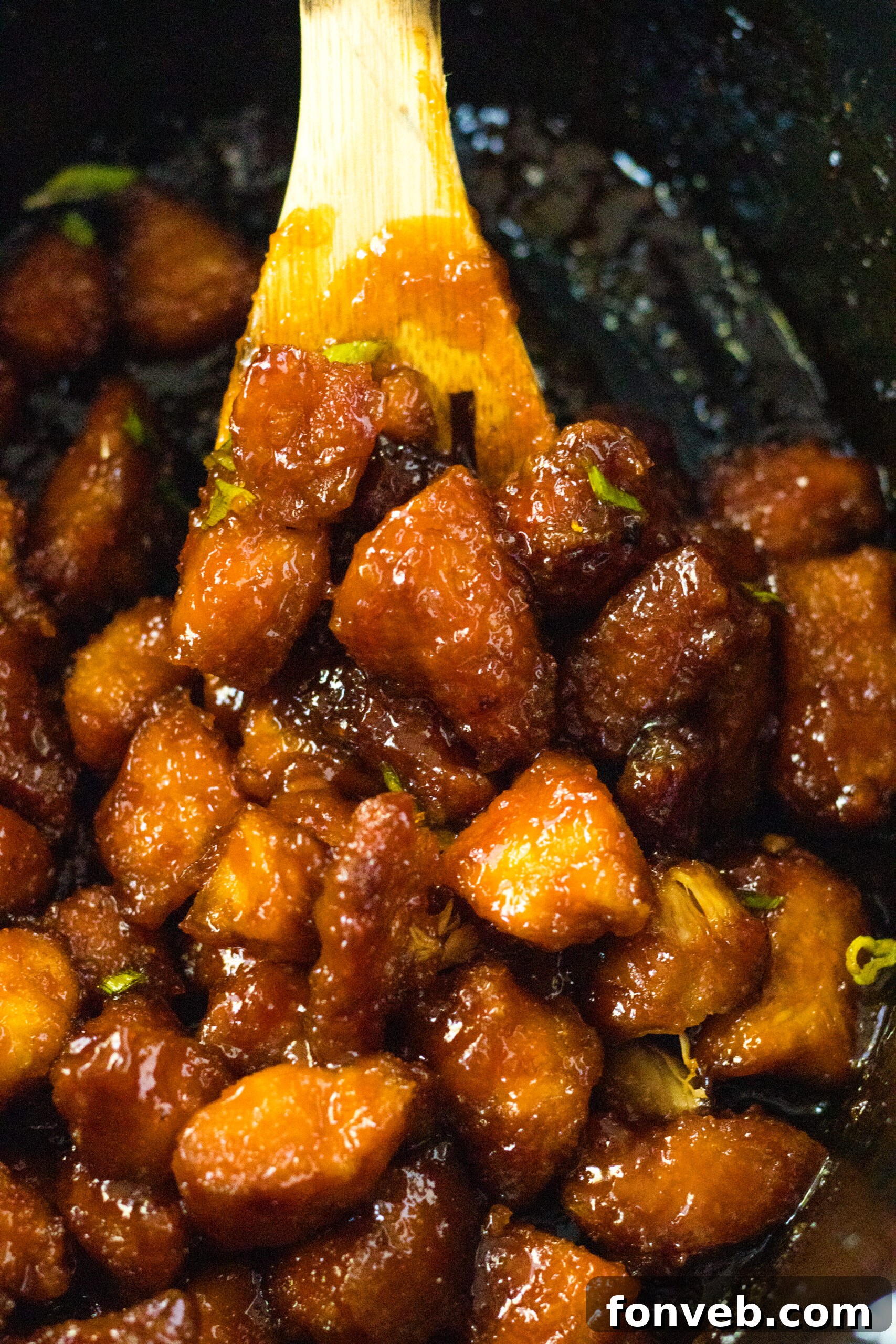 Close up view of a wooden spoon removing a generous serving of Slow Cooker Firecracker Chicken from the pot.