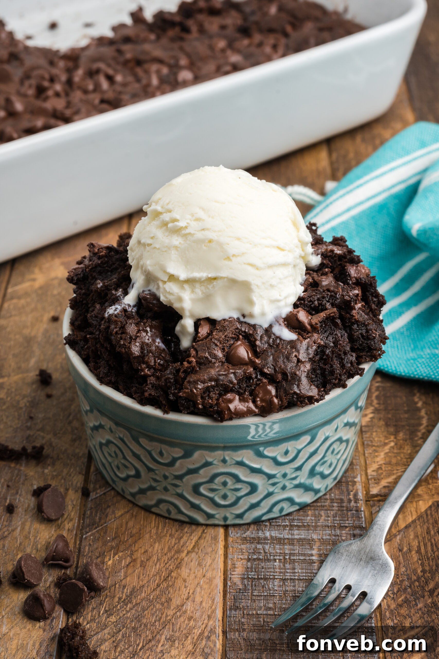 A generous serving of rich chocolate dump cake in a white bowl, topped with a scoop of melting vanilla ice cream, creating a delightful contrast.