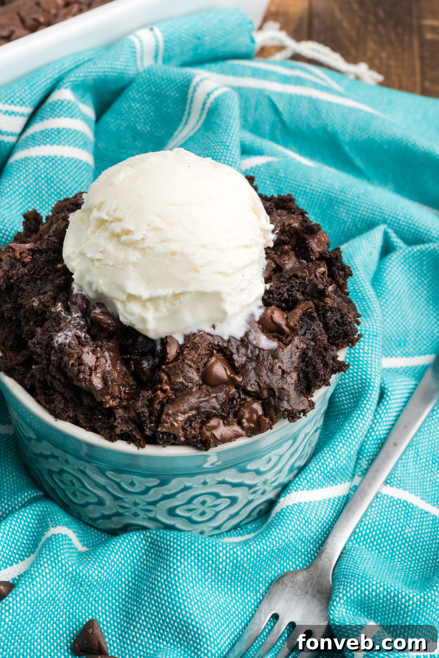 A close-up of a serving of chocolate dump cake in a white bowl, elegantly topped with a swirl of vanilla ice cream, showing off its enticing texture.