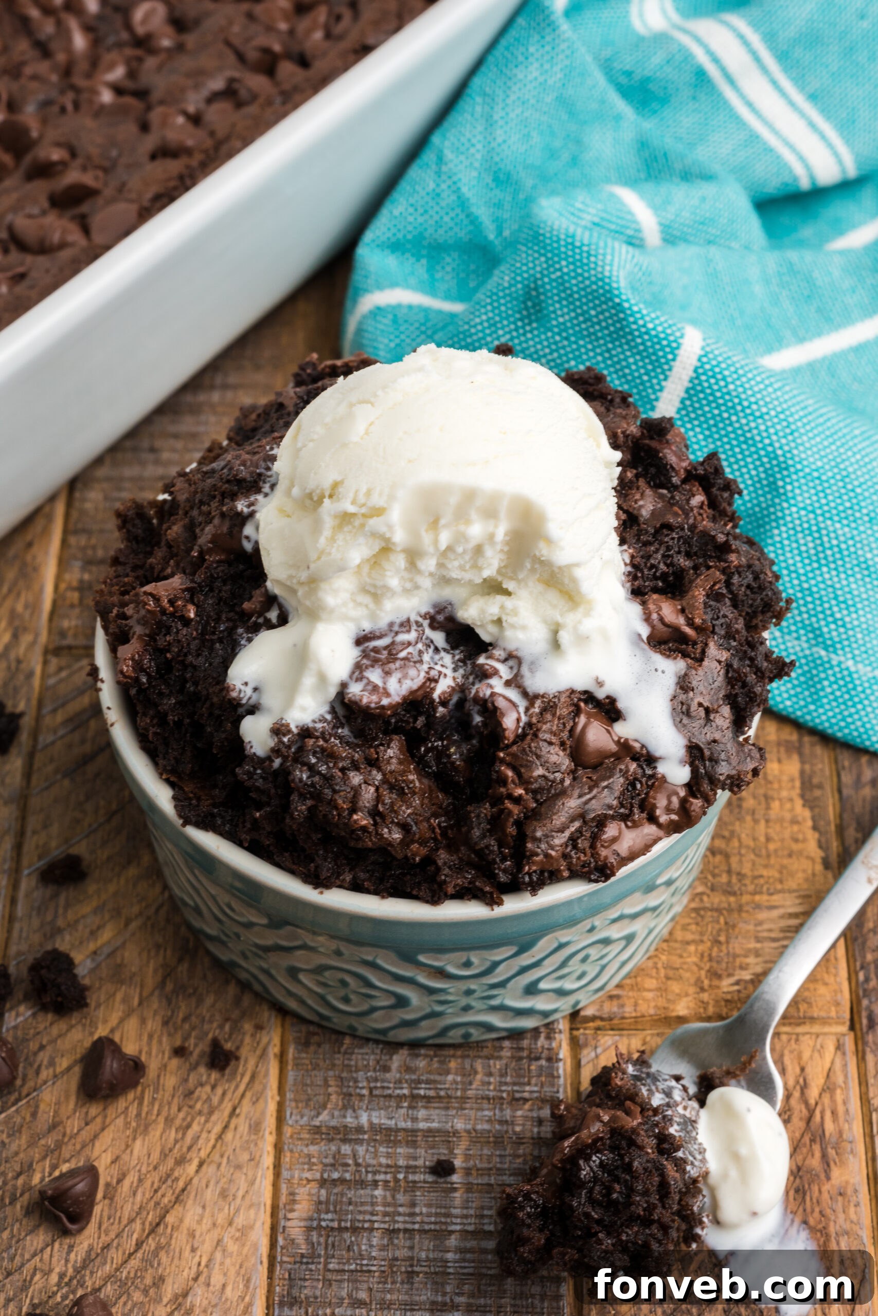 A serving of chocolate dump cake in a white bowl, with a bite already taken by a silver fork, inviting indulgence.