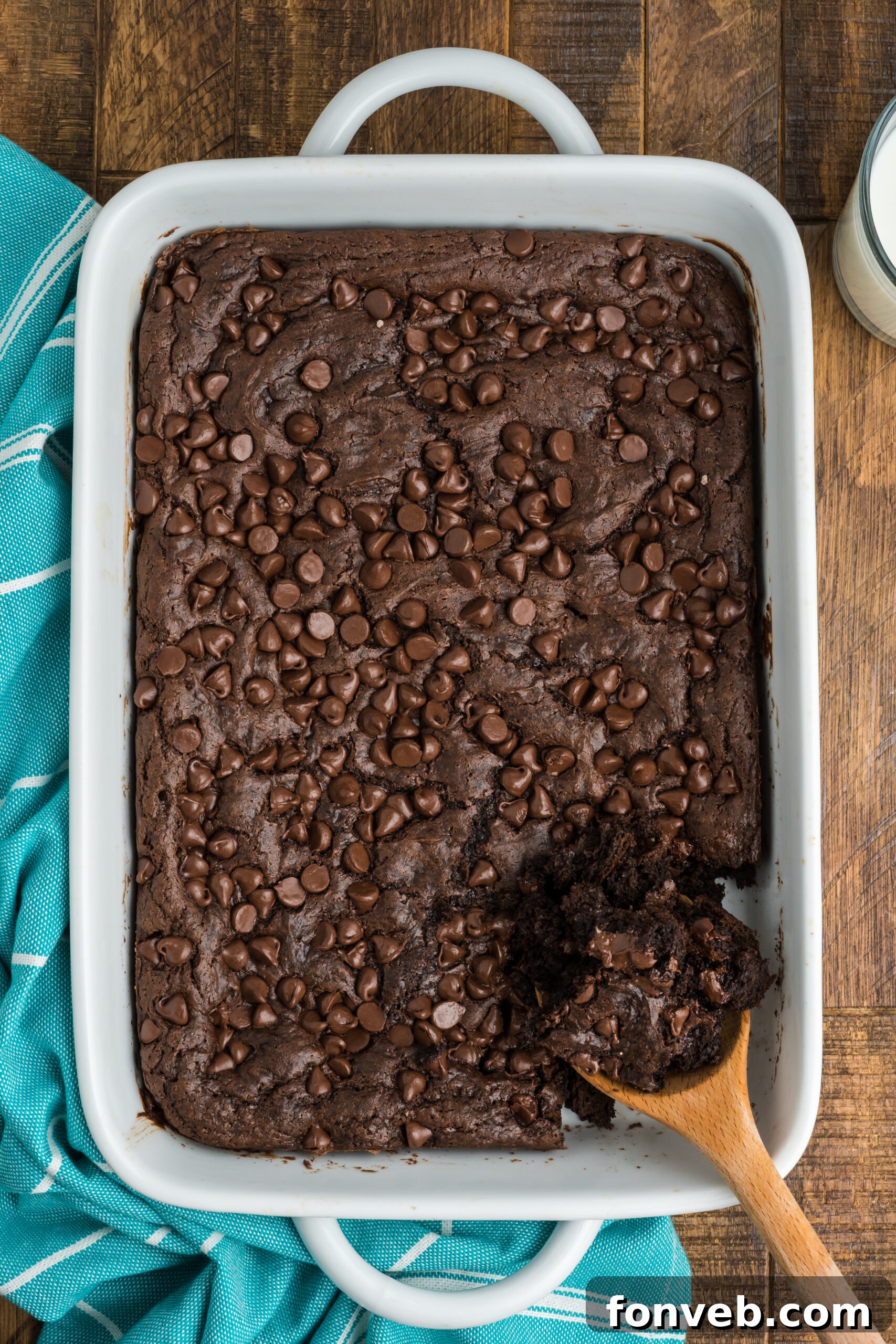 A wooden spoon carefully scoops a fudgy portion of chocolate dump cake from the white baking dish, highlighting its rich, moist texture.