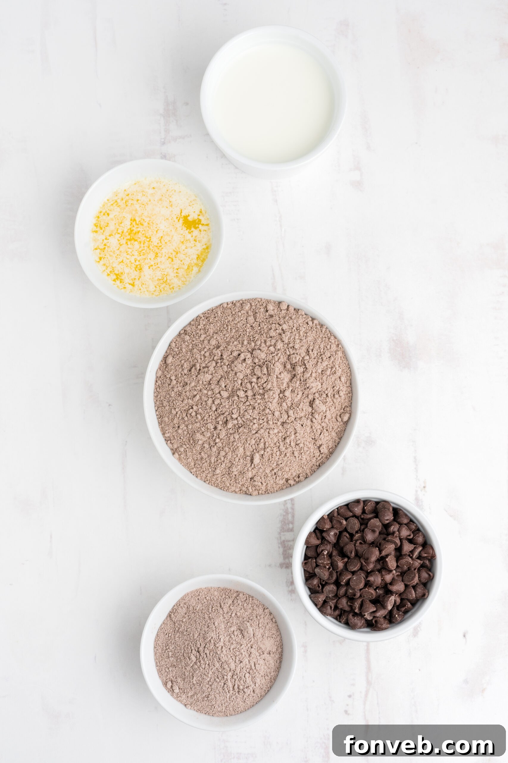 An overhead flat lay of all the essential ingredients laid out on a clean surface: a box of chocolate cake mix, instant chocolate pudding mix, butter, milk, and chocolate chips.