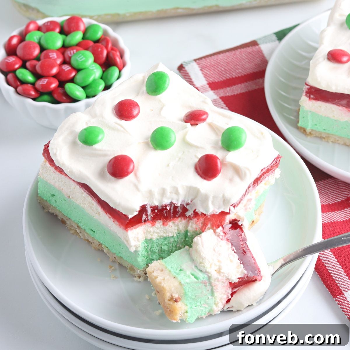 A slice of Christmas Lasagna dessert on a white plate with a fork taking a bite, showcasing the distinct layers.