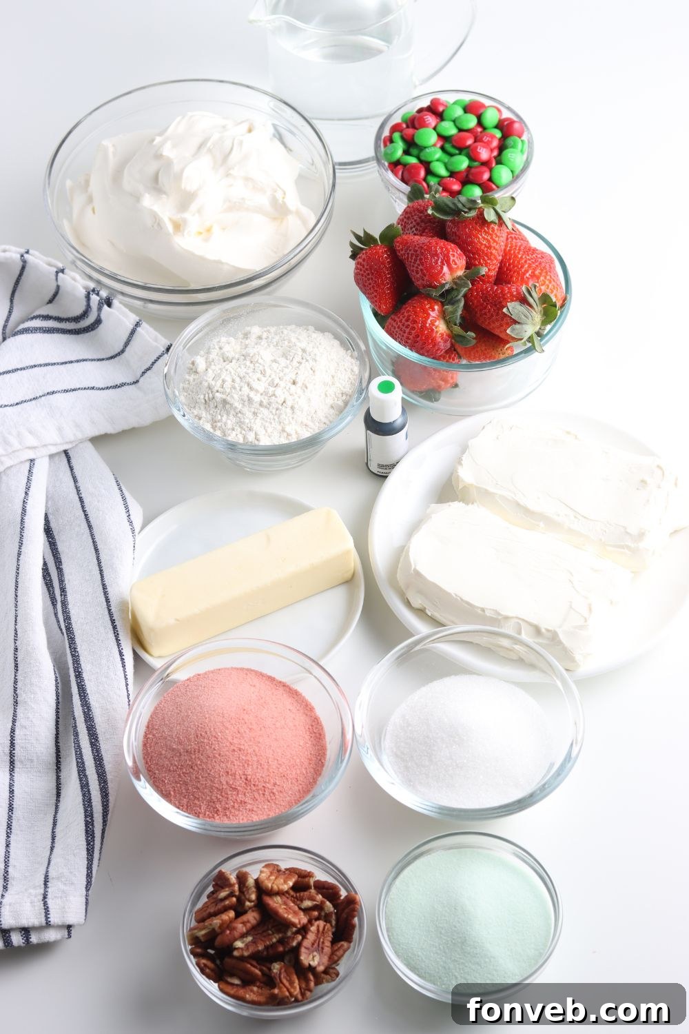 Various ingredients for the layered Christmas dessert displayed in small bowls on a wooden table.