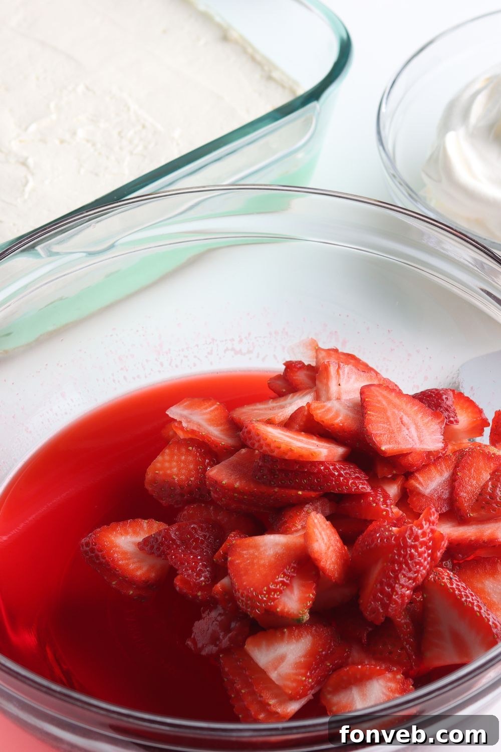Fresh strawberries mixed with red Jello in a glass bowl.
