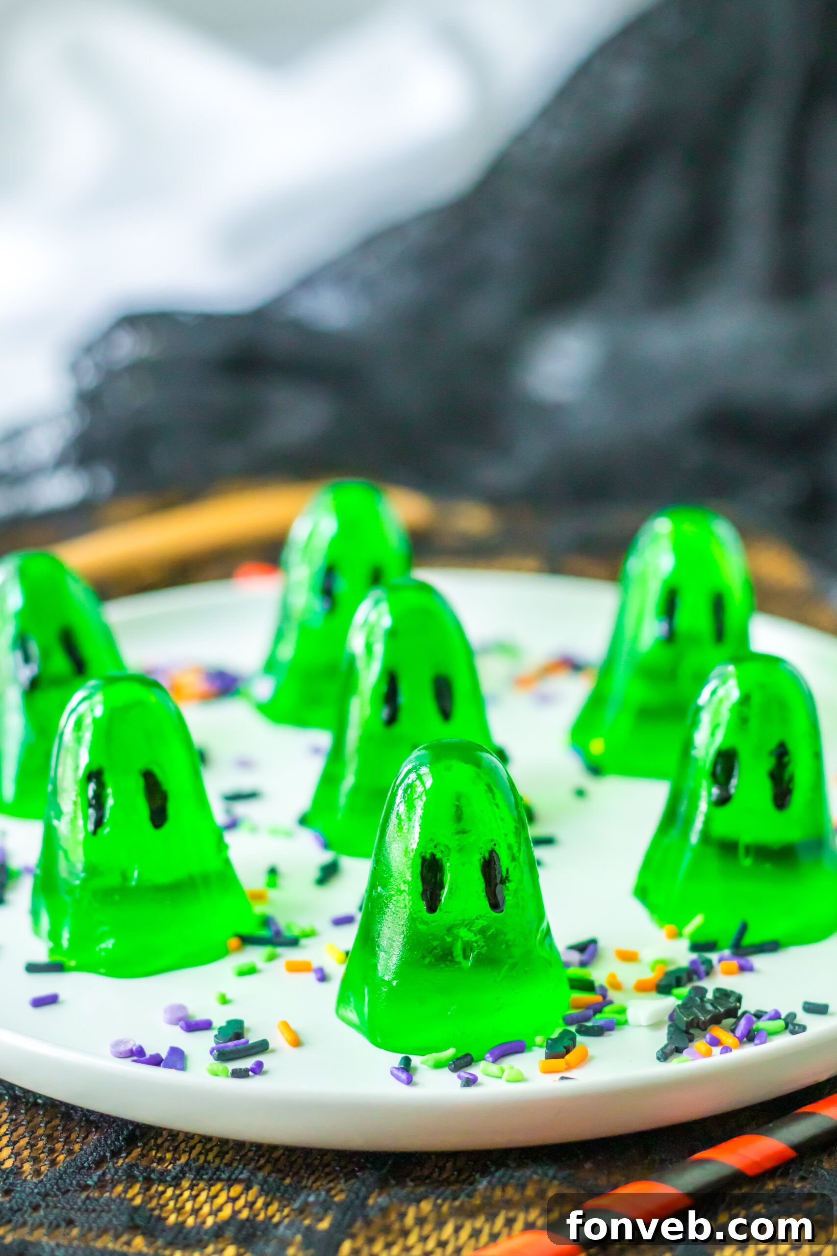 Spooky Spirit Shooters 13 A display of shimmering green jello shots in ghost shapes, artfully arranged on a white plate, perfect for a Halloween celebration.