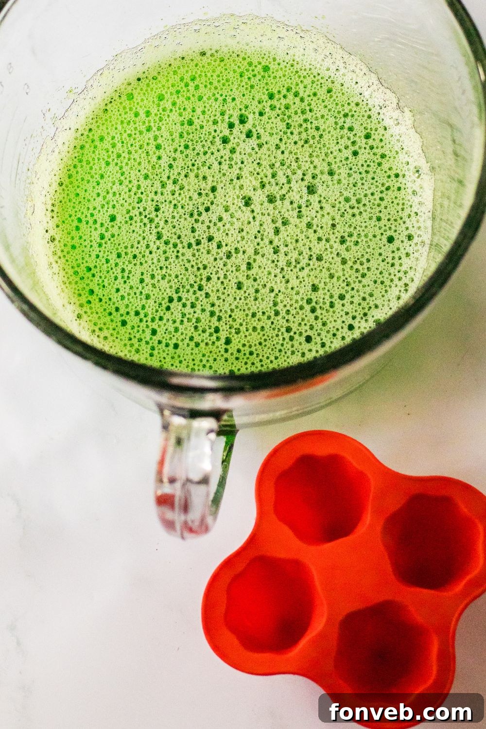 Spooky Spirit Shooters 5 A ghost-shaped silicone mold placed on a table, with a measuring cup filled with jello mixture beside it, ready for pouring.