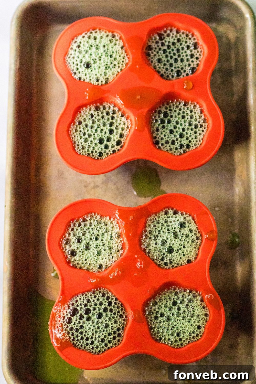 Spooky Spirit Shooters 6 Multiple ghost-shaped silicone molds, neatly arranged on a baking sheet, freshly filled with green jello mixture.