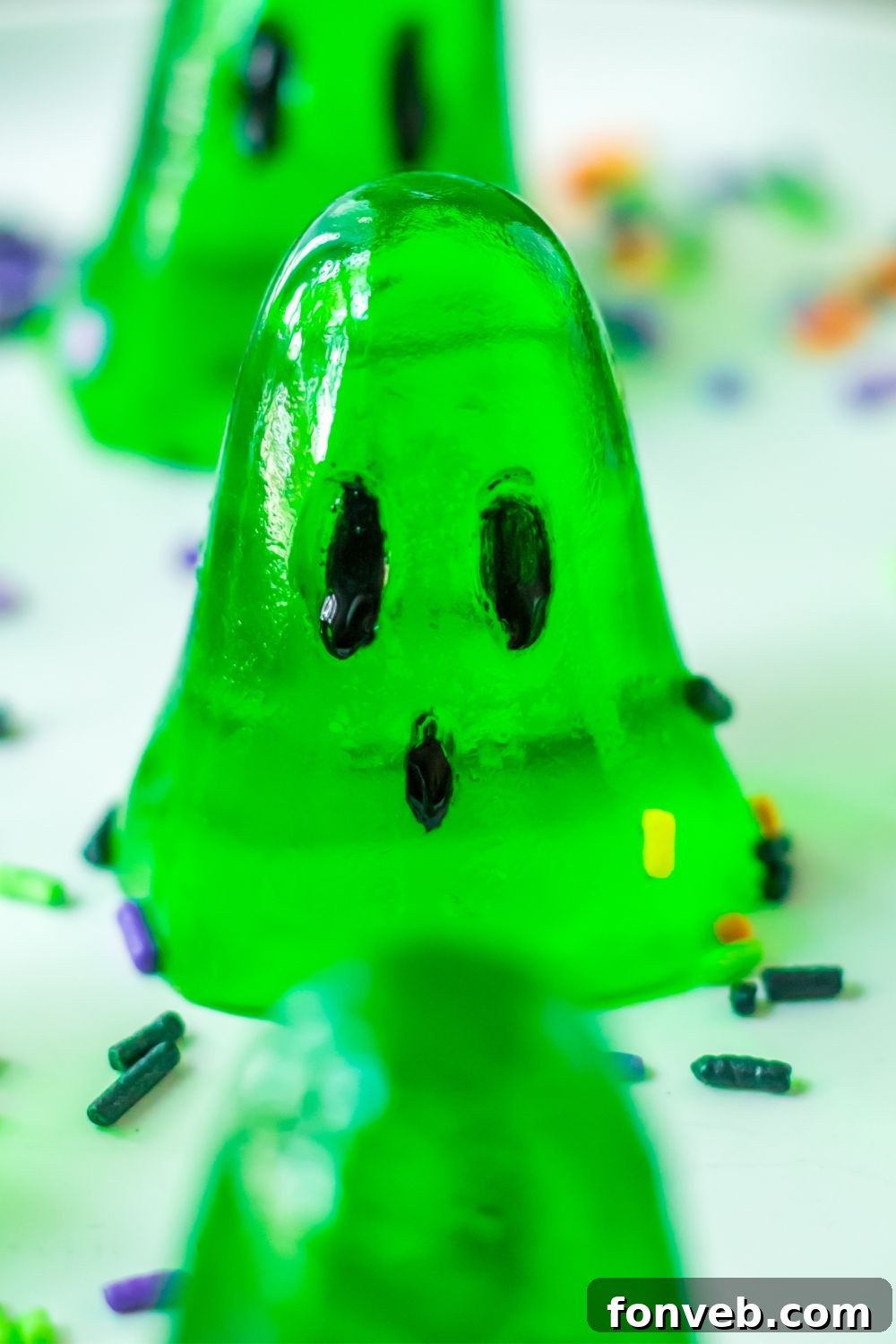 Spooky Spirit Shooters 8 A close-up of a single vibrant green ghost-shaped jello shot on a plate, surrounded by playful Halloween sprinkles.