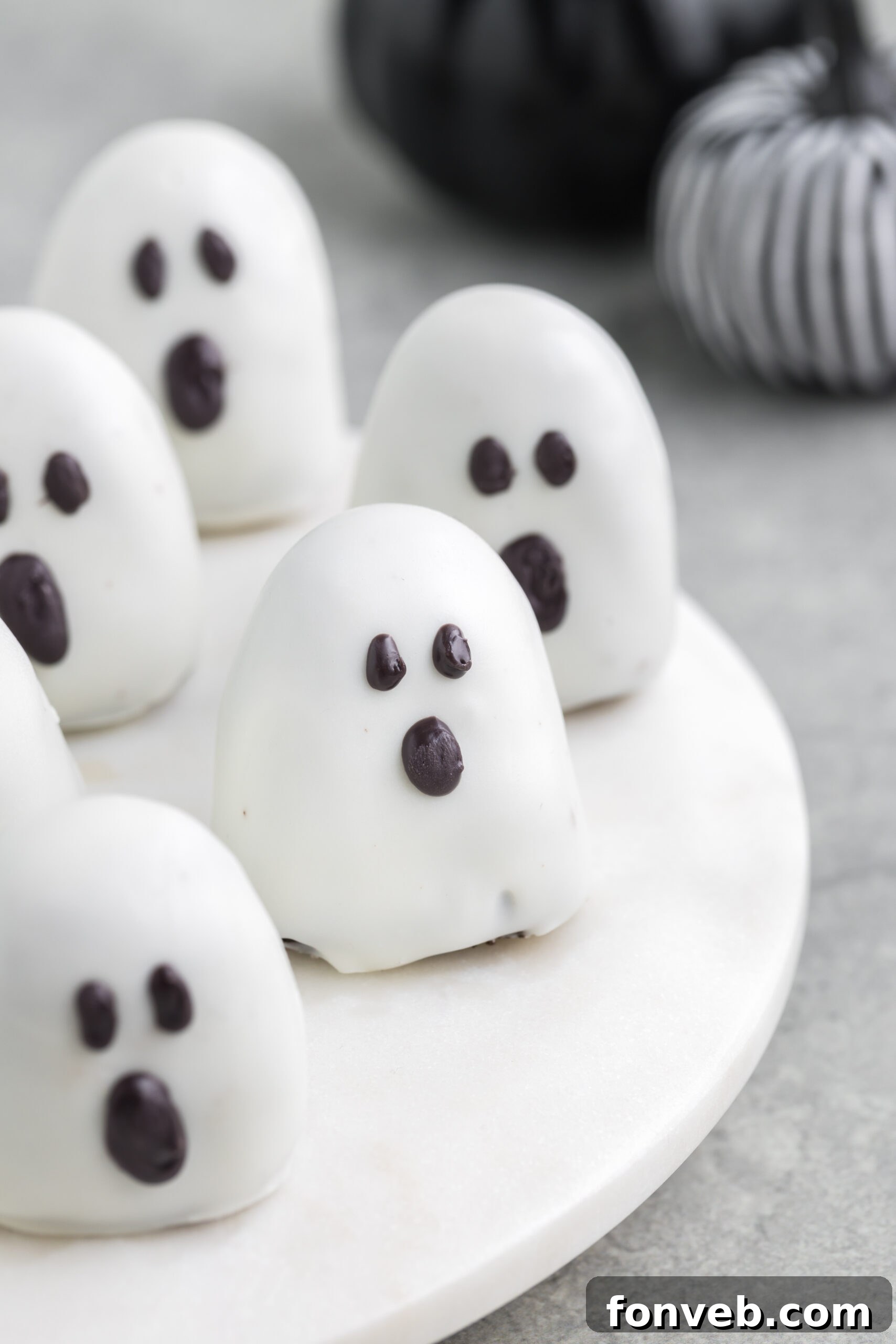 Spooky Oreo truffles on a white marble serving platter with fabric pumpkins behind them