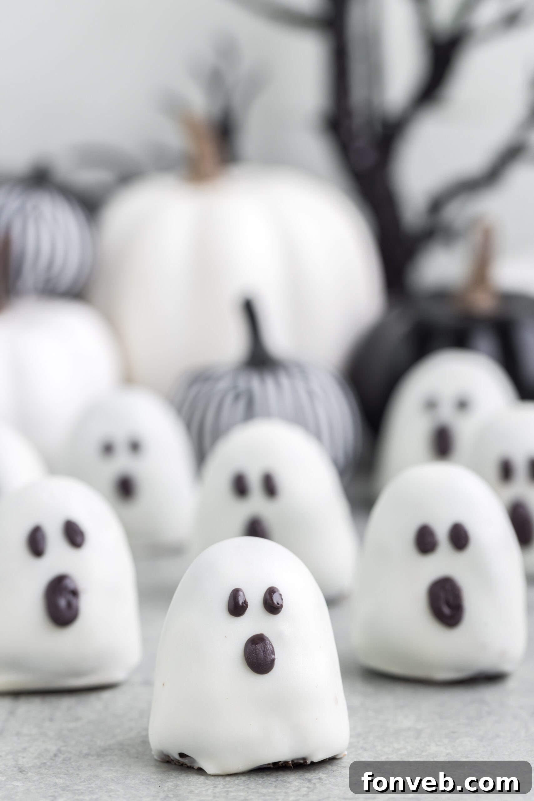 Spooky Oreo truffles on a grey table with fabric pumpkins behind them