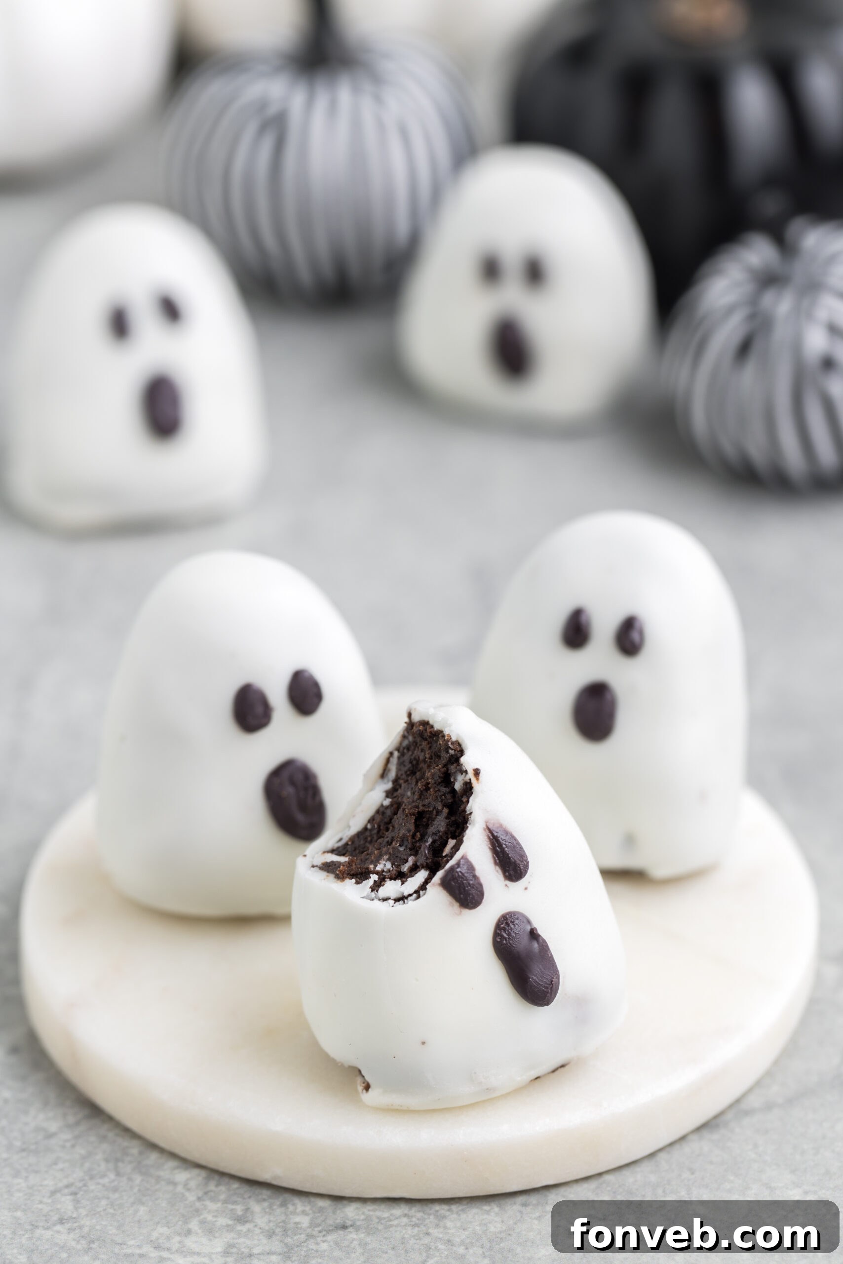 An Oreo ghost truffle with a bite taken out, sitting on a platter on a table