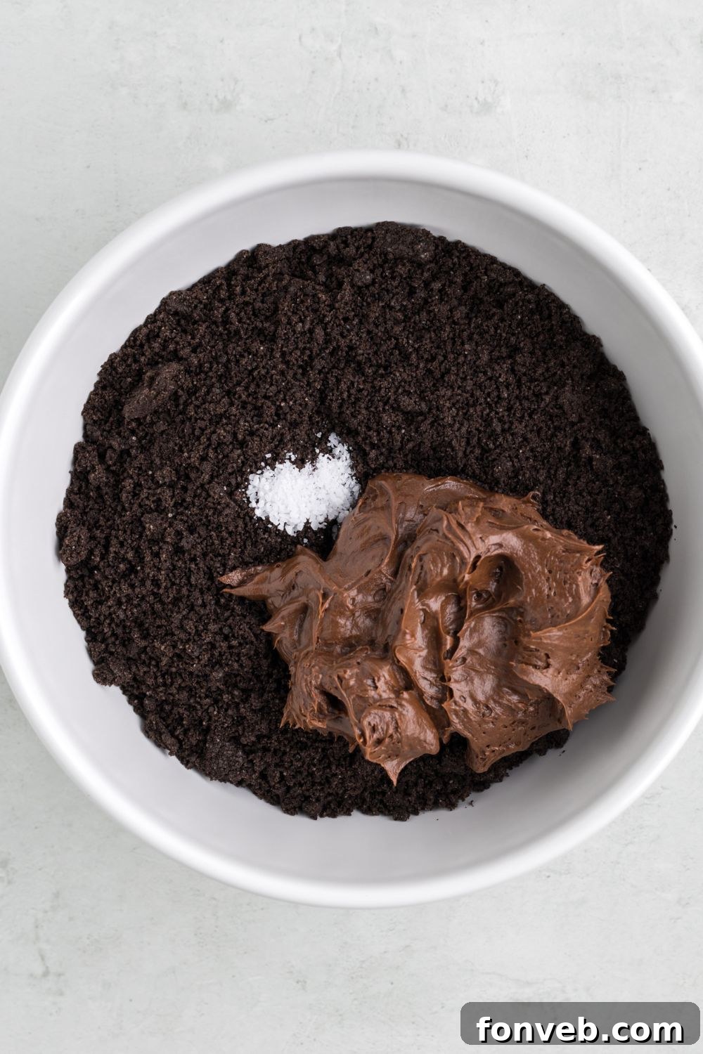 Crushed Oreos in a bowl topped with chocolate frosting and a little salt