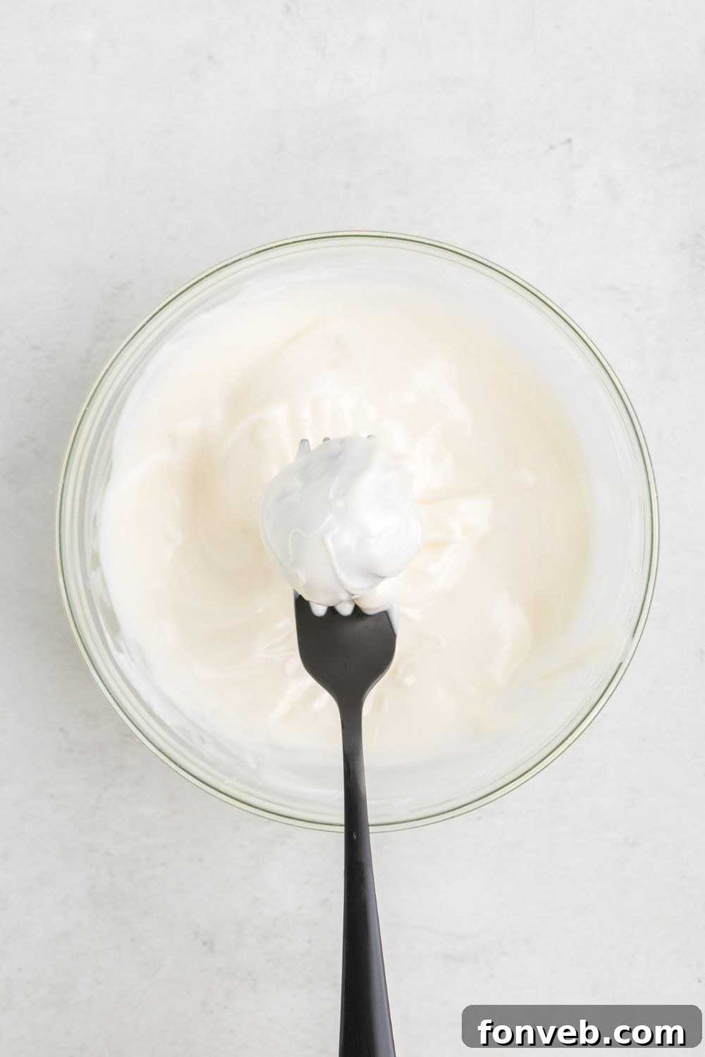 Oreo ball dipped in white chocolate being held with a fork above the bowl
