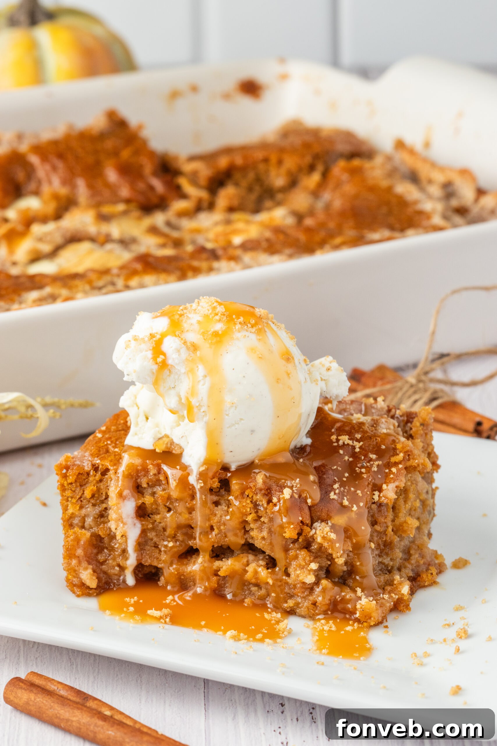 Pumpkin Earthquake Cake on a white plate with a scoop of vanilla ice cream on top then drizzled with caramel sauce