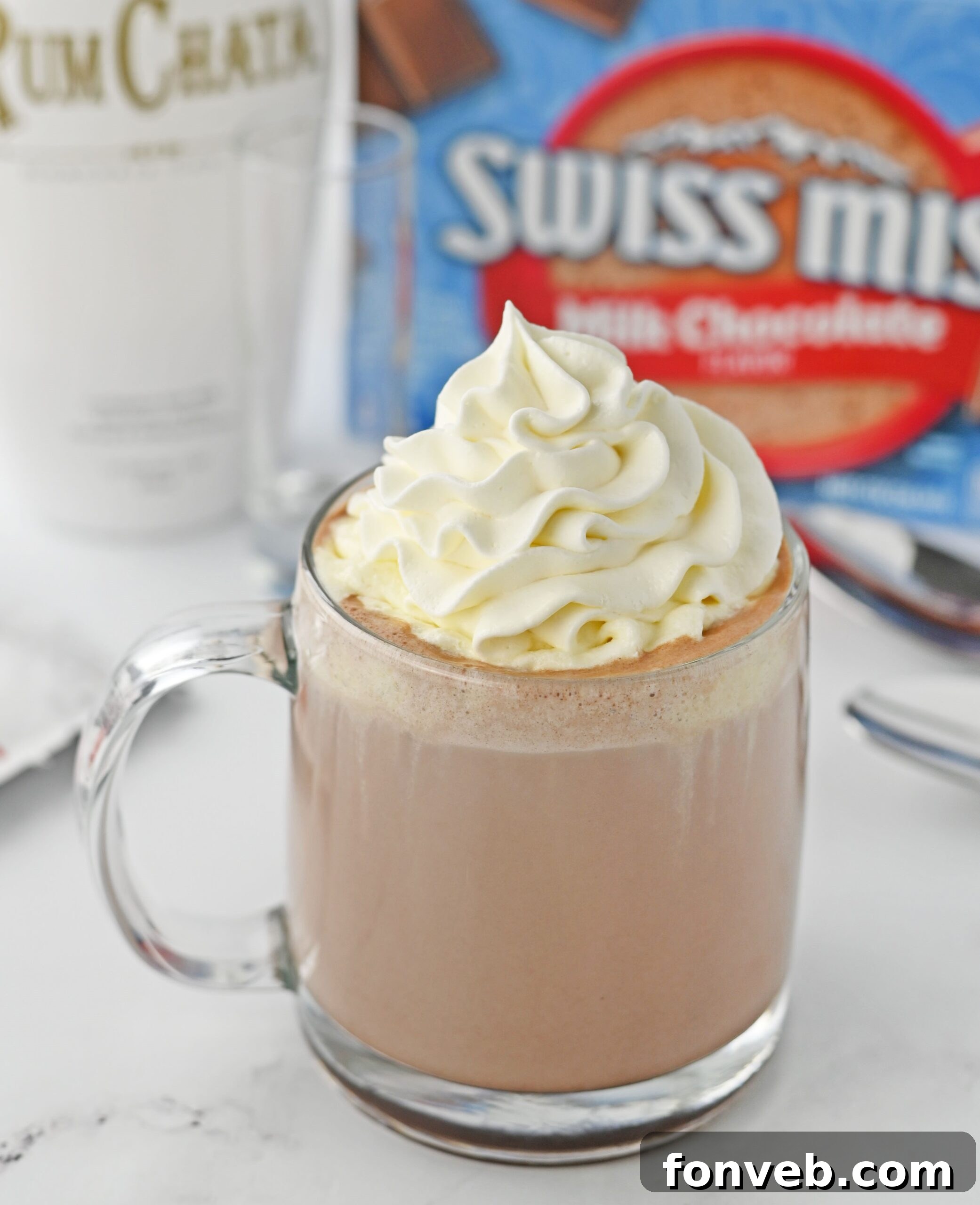 RumChata hot chocolate in a clear glass mug, topped with a generous swirl of whipped cream and a sprinkle of cinnamon