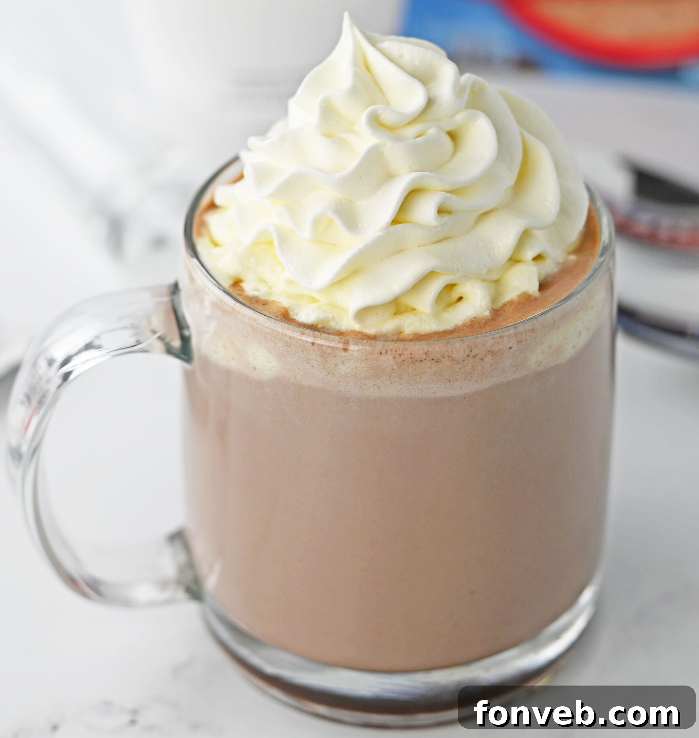 Up-close shot of a clear glass mug of RumChata hot chocolate, richly topped with whipped cream, highlighting the smooth texture and appealing presentation