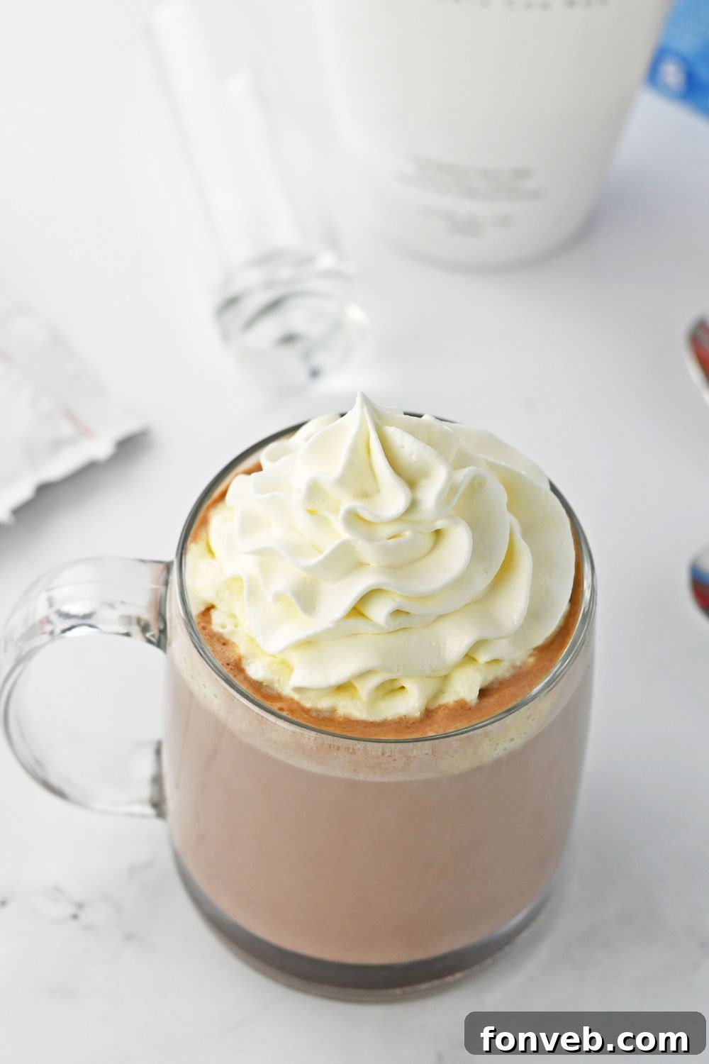 Finished RumChata hot chocolate, topped with whipped cream, presented in a clear glass mug on a white table