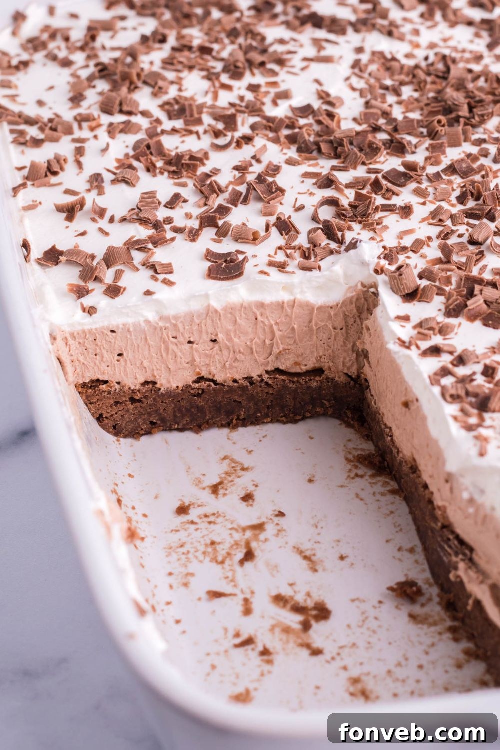 layered brownie dessert in pan with some pieces cut out to showcase the layers