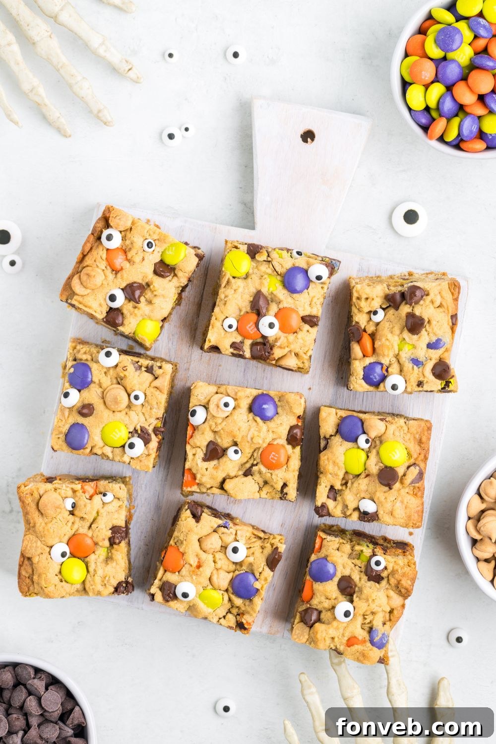 Cookie bars scattered on a table with Halloween decorations and a bowl of M&M's, creating a festive arrangement.
