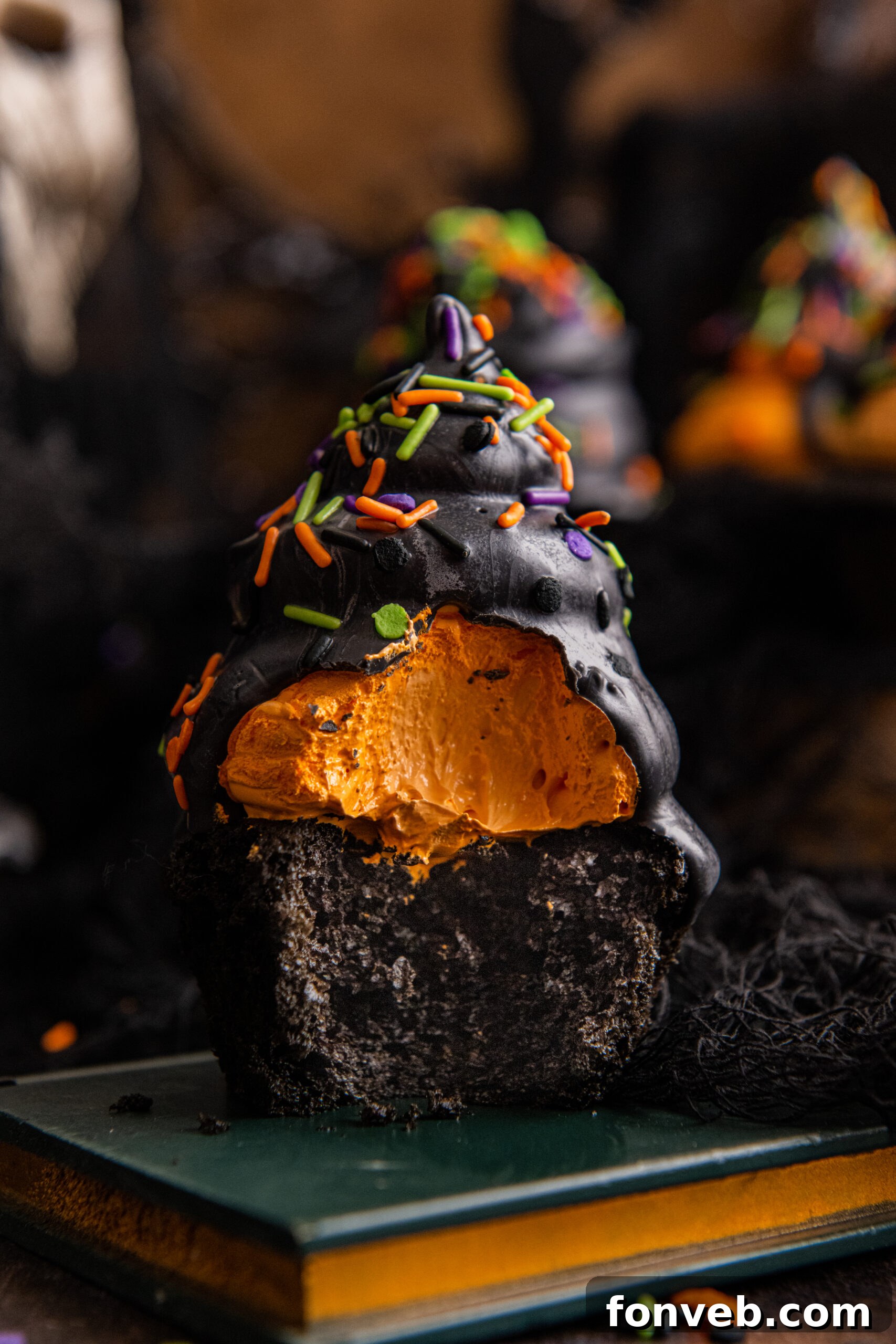 Bite taken out of a Halloween cupcake on a book, showcasing the black cake and orange marshmallow fluff.