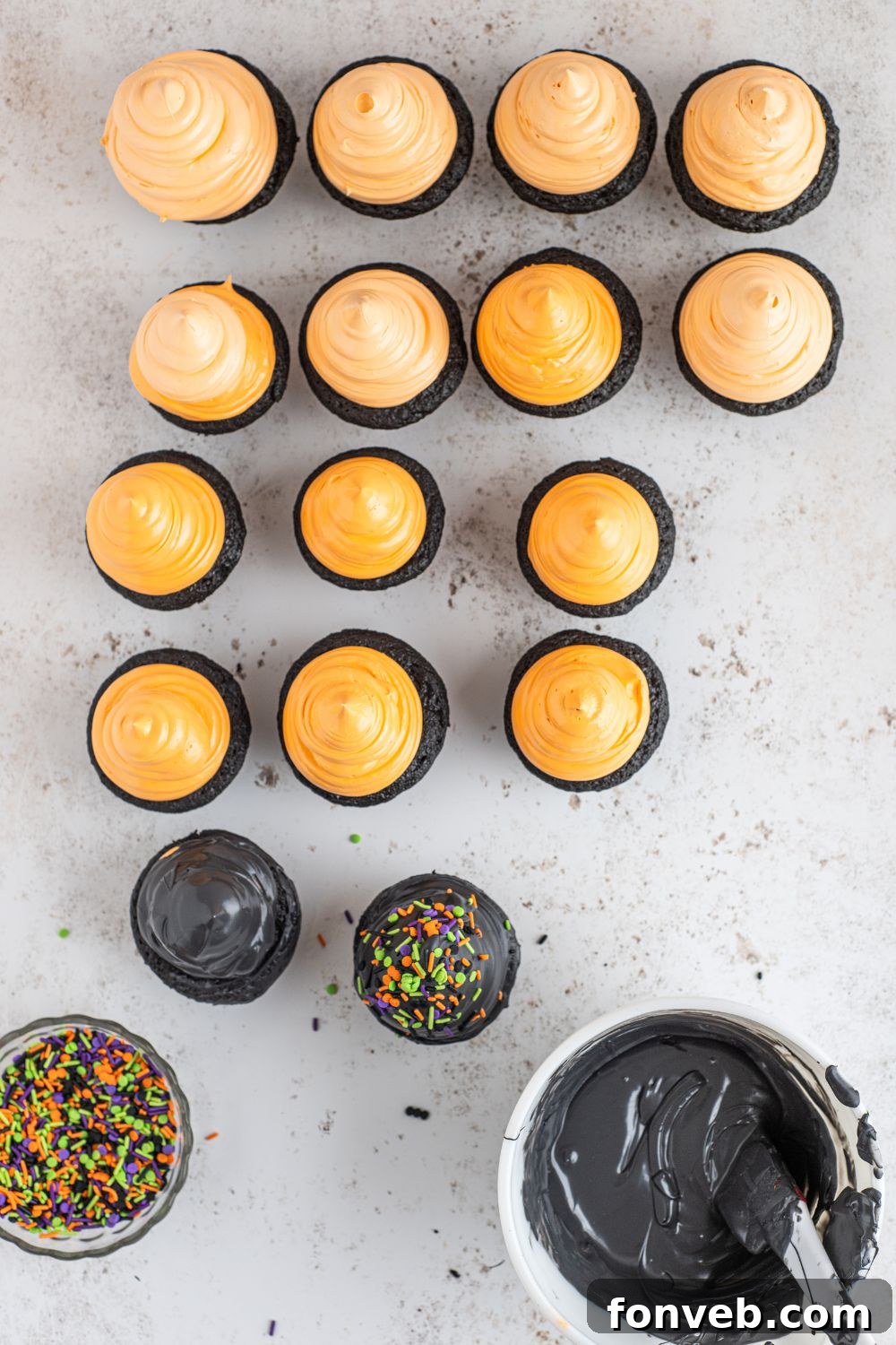 Orange marshmallow frosted cupcakes on a counter, waiting for the chocolate dip.