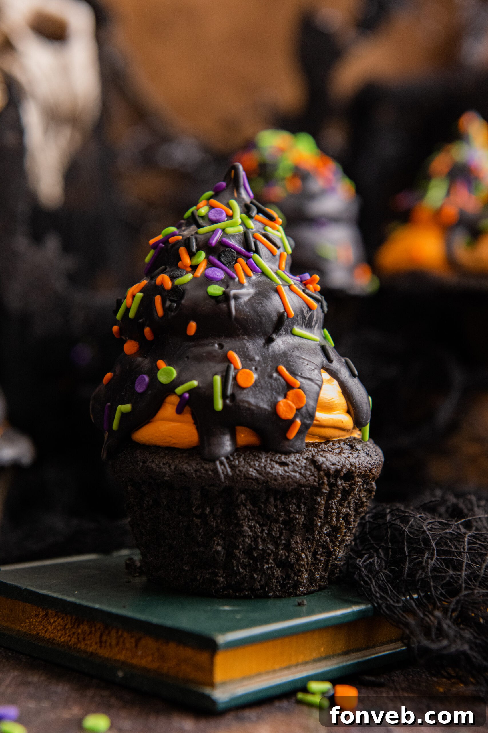 Close up view of a Halloween cupcake on stacked books, emphasizing the texture of the marshmallow fluff and sprinkles.
