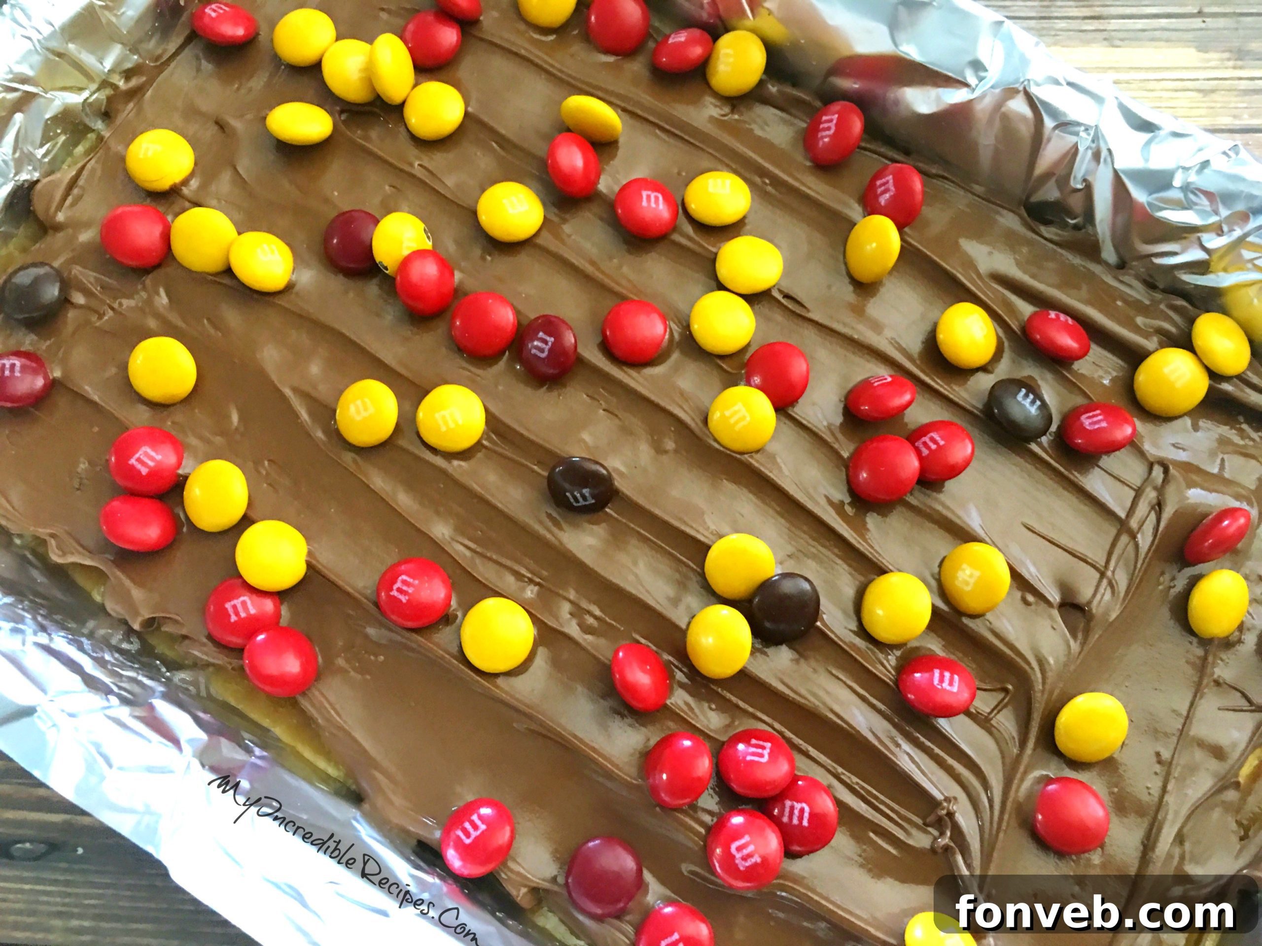 Freshly sprinkled M&Ms on a sheet of chocolate and toffee covered crackers, cooling