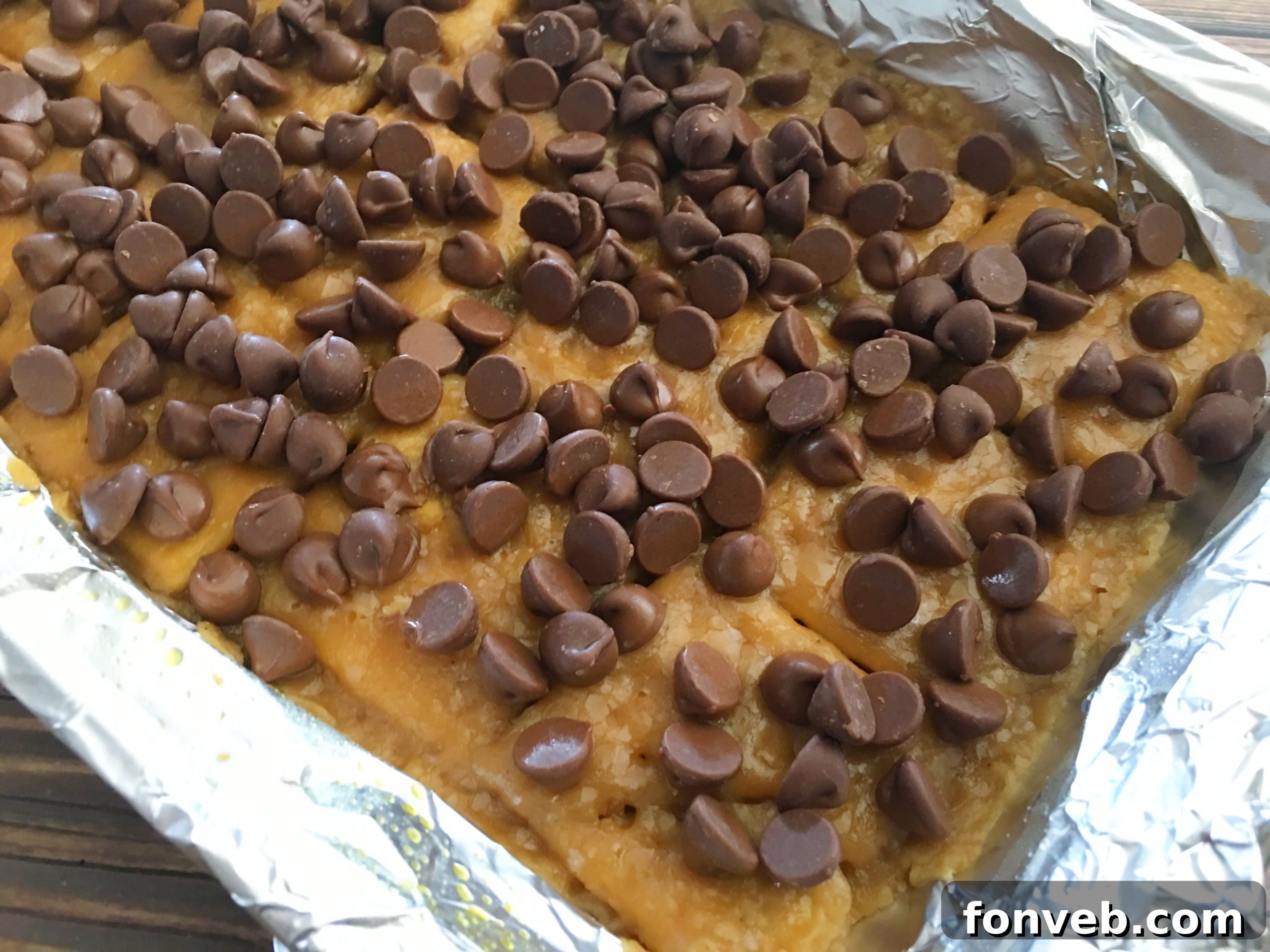 Chocolate chips sprinkled over hot toffee-coated saltine crackers in a baking pan