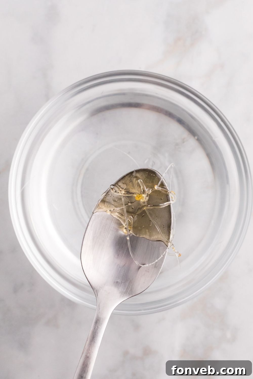 spoon with hardened candy coating on it above a bowl of water 