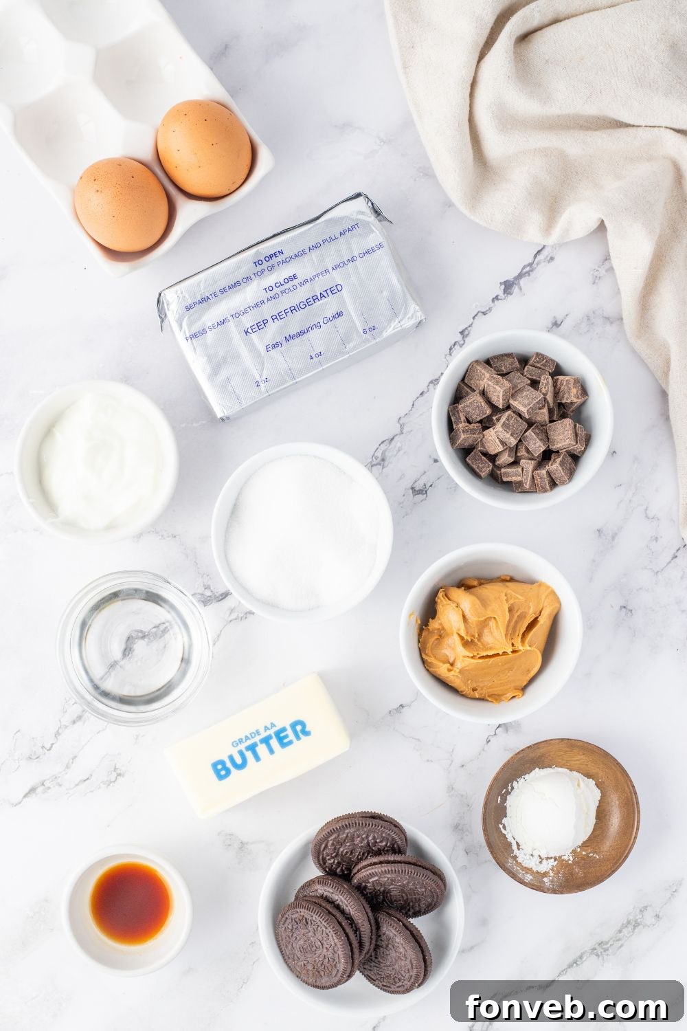 A collection of ingredients for peanut butter cheesecake, including Oreos, cream cheese, peanut butter, and eggs, arranged on a marble countertop.