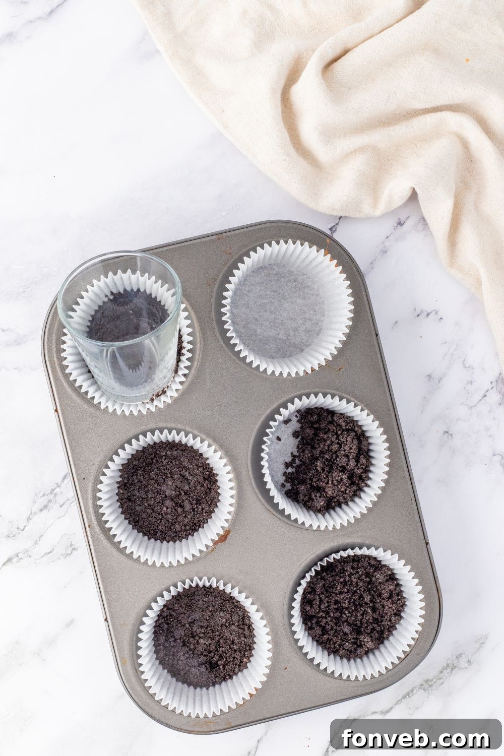 An Oreo cookie crust being pressed into a muffin tin lined with cupcake wrappers.
