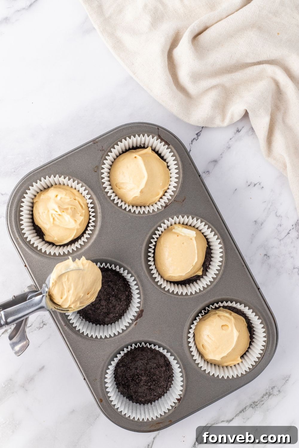 Peanut butter cheesecake filling being spooned into muffin tin liners with pre-baked crusts.