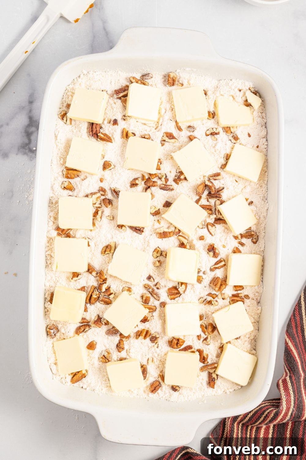 Thin slices of cold butter meticulously arranged in an even layer across the top of the dry cake mix and pecans in the baking dish, crucial for the crumb topping.