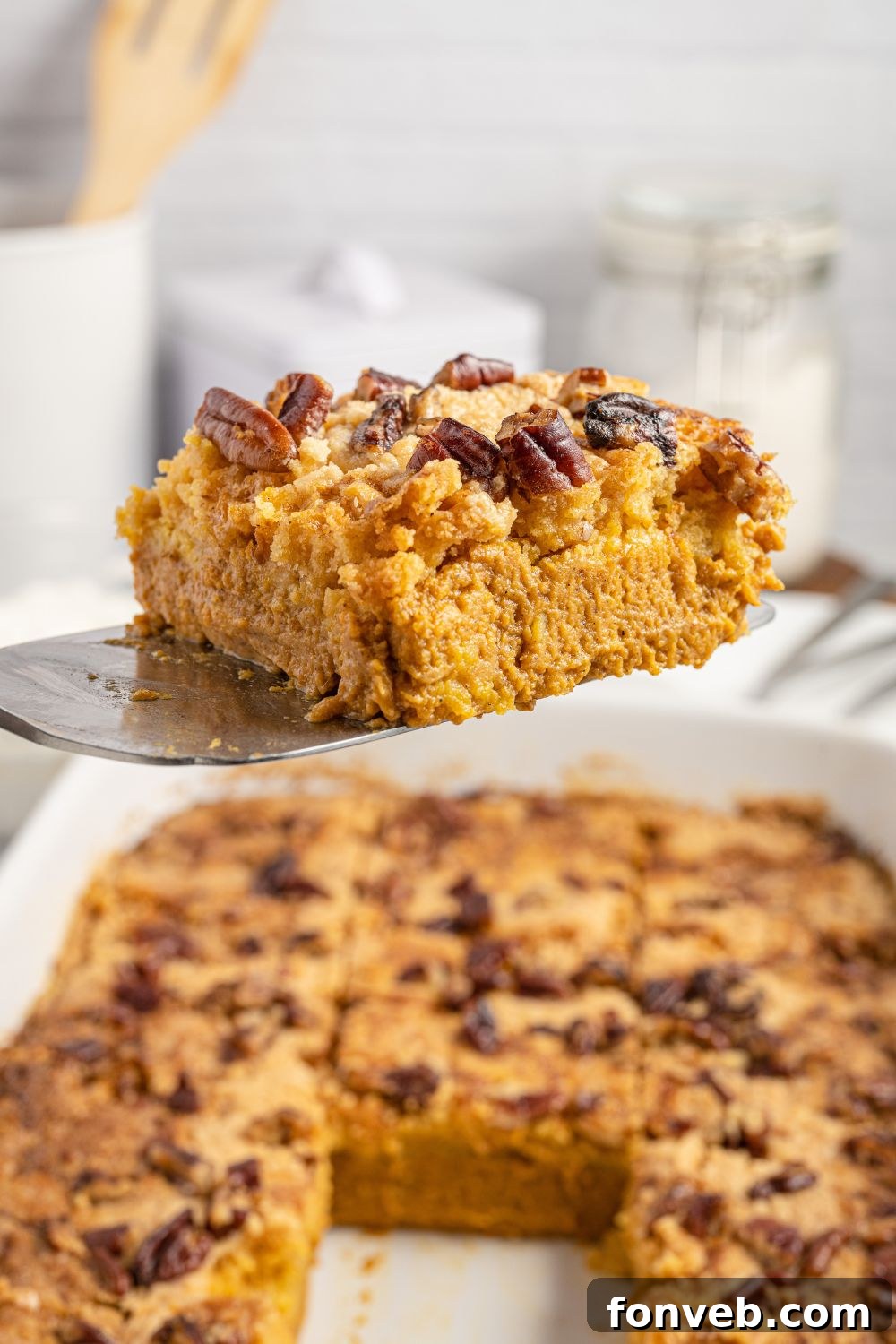 A spatula lifting a perfect slice of warm Pumpkin Dump Cake from a baking pan, showing the distinct layers of creamy pumpkin and golden cake topping.