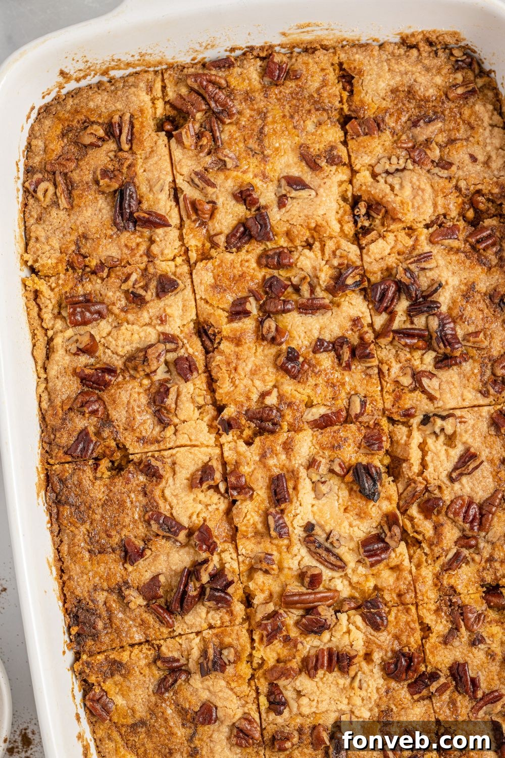 An overhead shot of a baked Pumpkin Dump Cake in its pan, featuring a golden-brown, crumbly top with distinct squares cut, ready for serving.