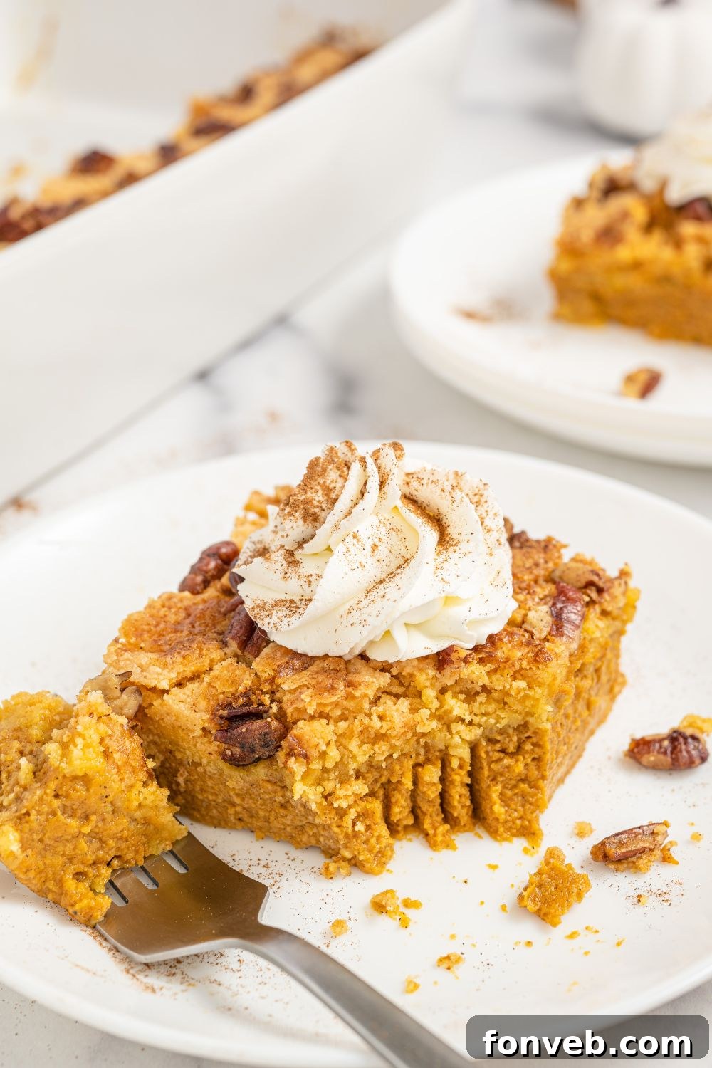 A close-up of a slice of Pumpkin Dump Cake on a white plate, with a fork holding a bite-sized piece, revealing the moist cake and creamy pumpkin layers.