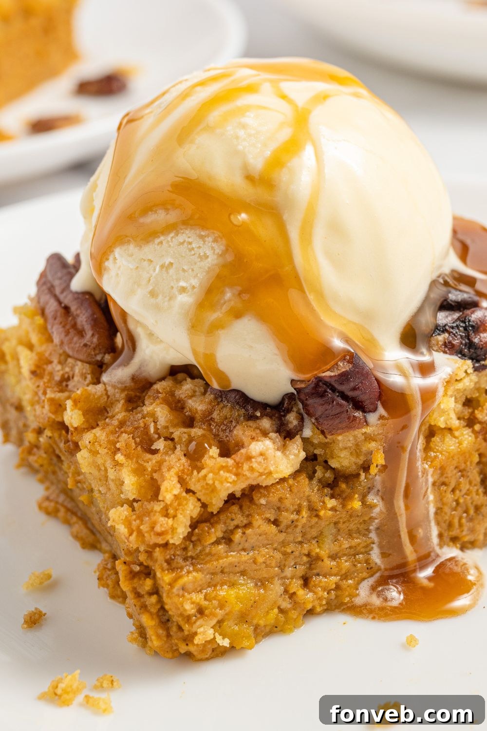 A tempting slice of Pumpkin Dump Cake on a white plate, artfully topped with a scoop of vanilla ice cream and a luscious caramel sauce drizzle.