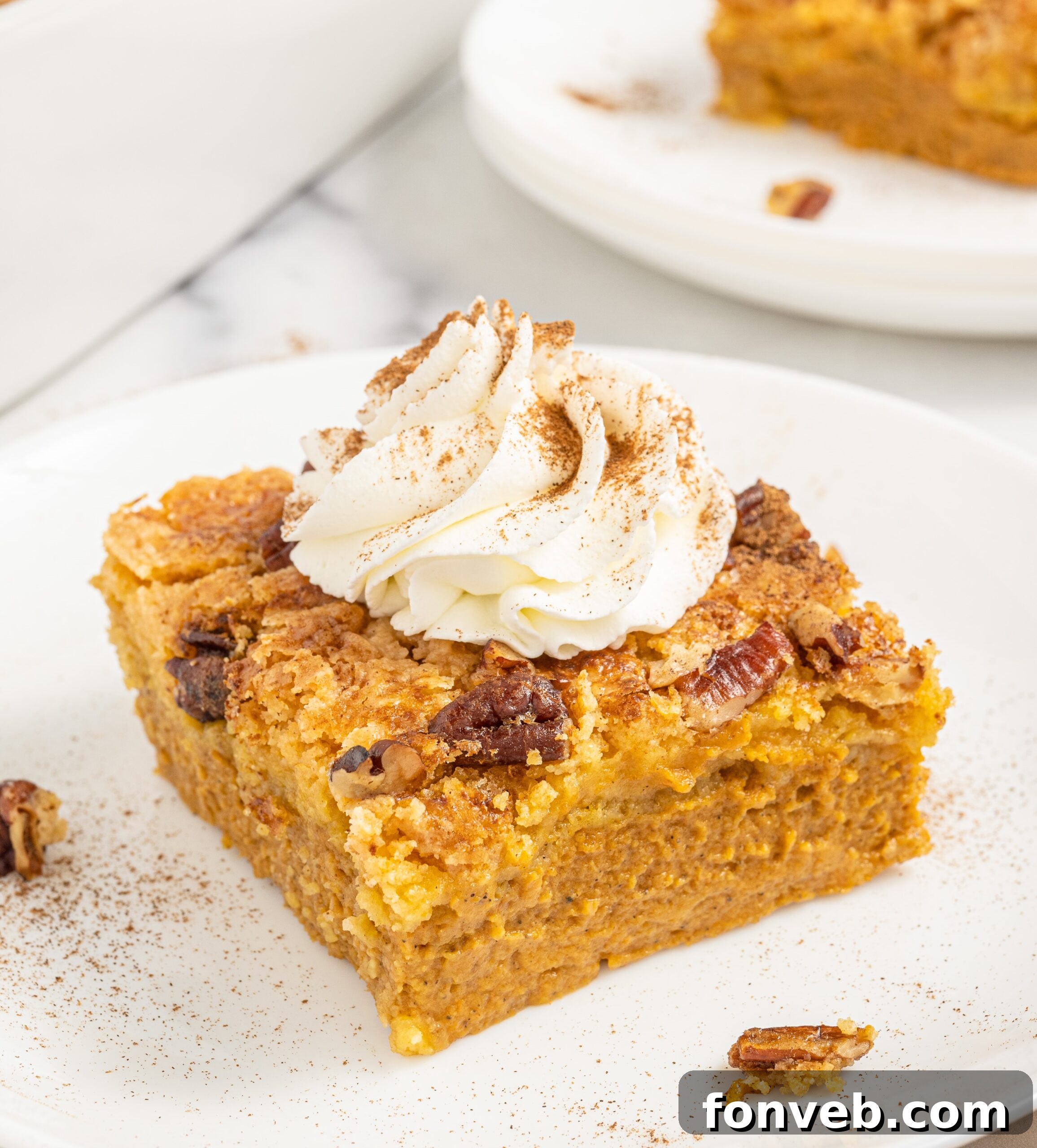 A whole Pumpkin Dump Cake in a ceramic baking dish, with several slices already served, showcasing the golden cake topping and the creamy pumpkin layer beneath.
