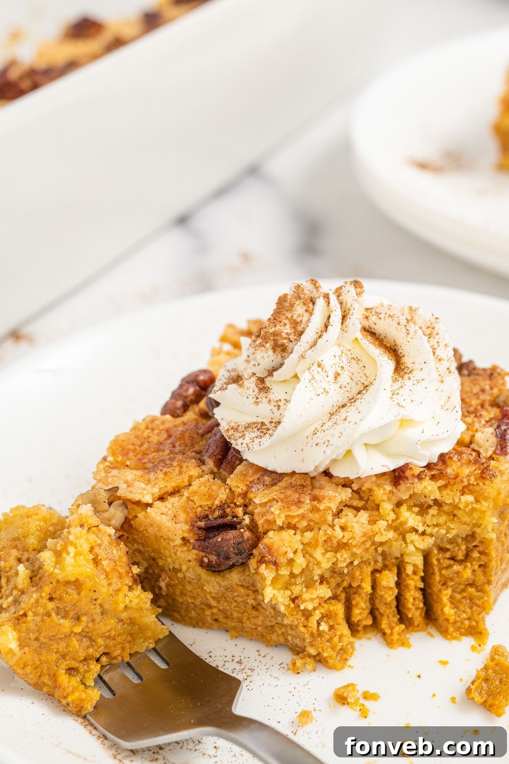 A close-up of a slice of Pumpkin Dump Cake on a white plate, with a bite taken out, highlighting the moist texture and inviting layers.