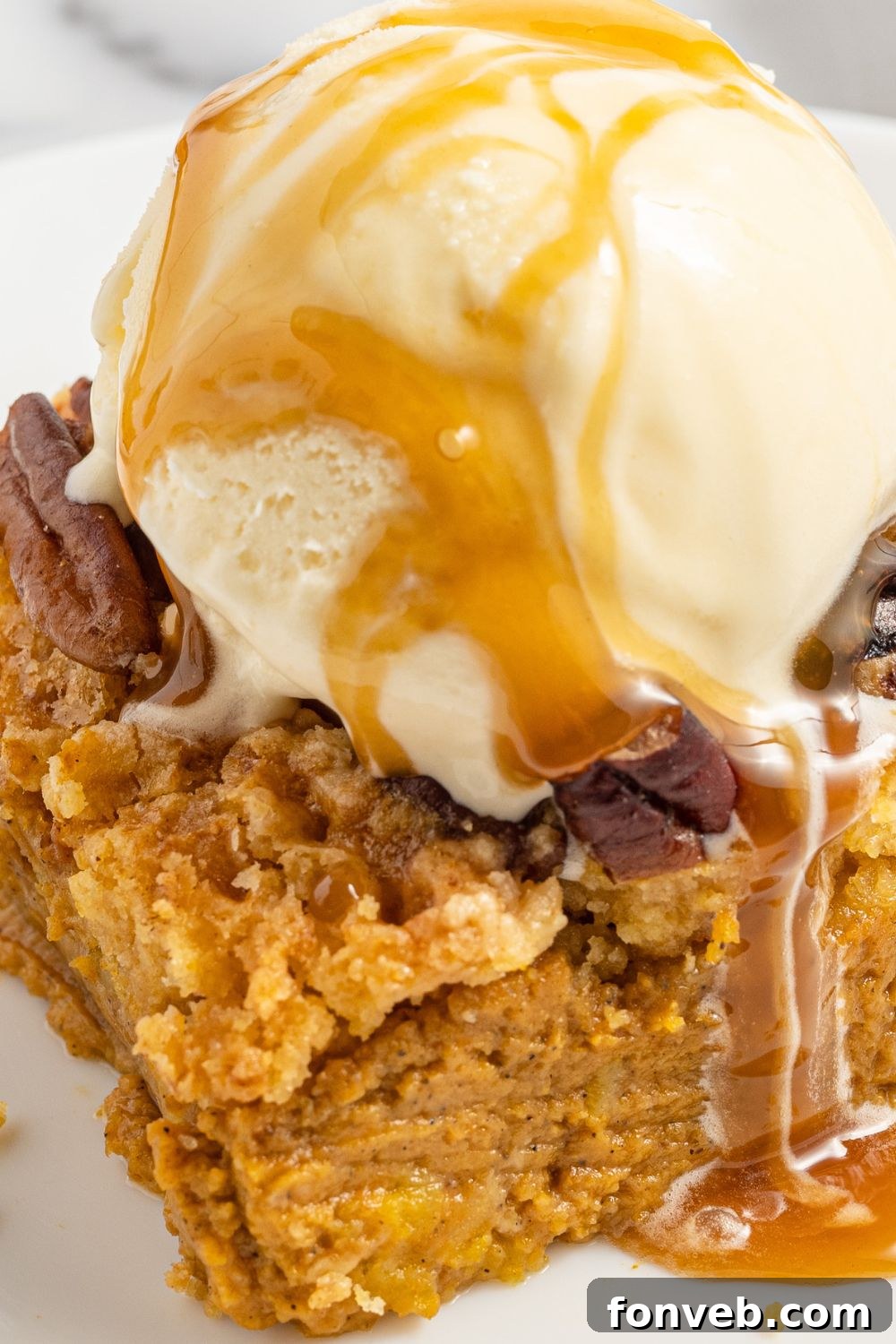 A close-up side view of a slice of Pumpkin Dump Cake, served with a melting scoop of ice cream on top, highlighting the creamy and cake layers.