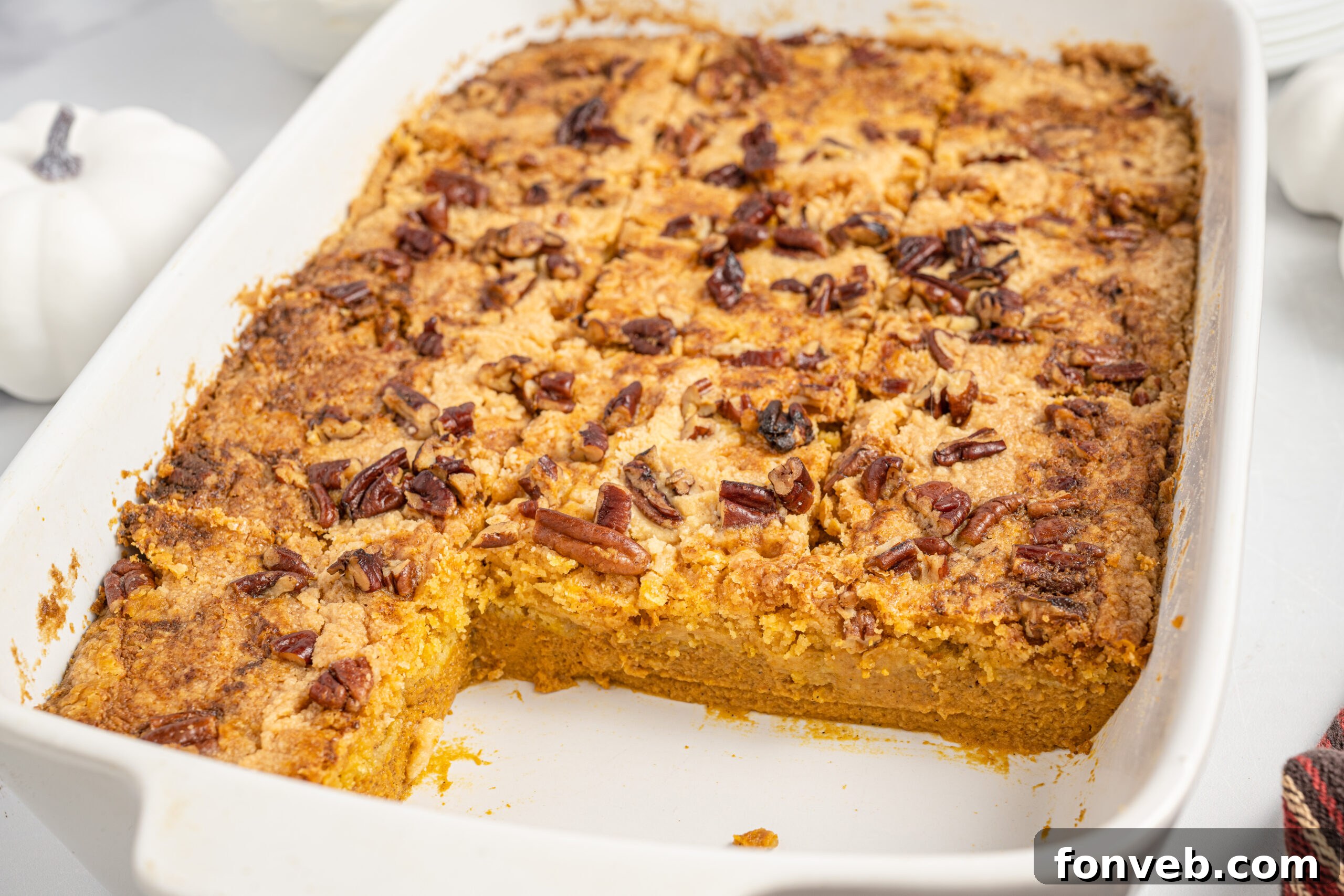An overhead view of a freshly baked Pumpkin Dump Cake in a white rectangular baking dish, with a few slices neatly cut and ready to be served.