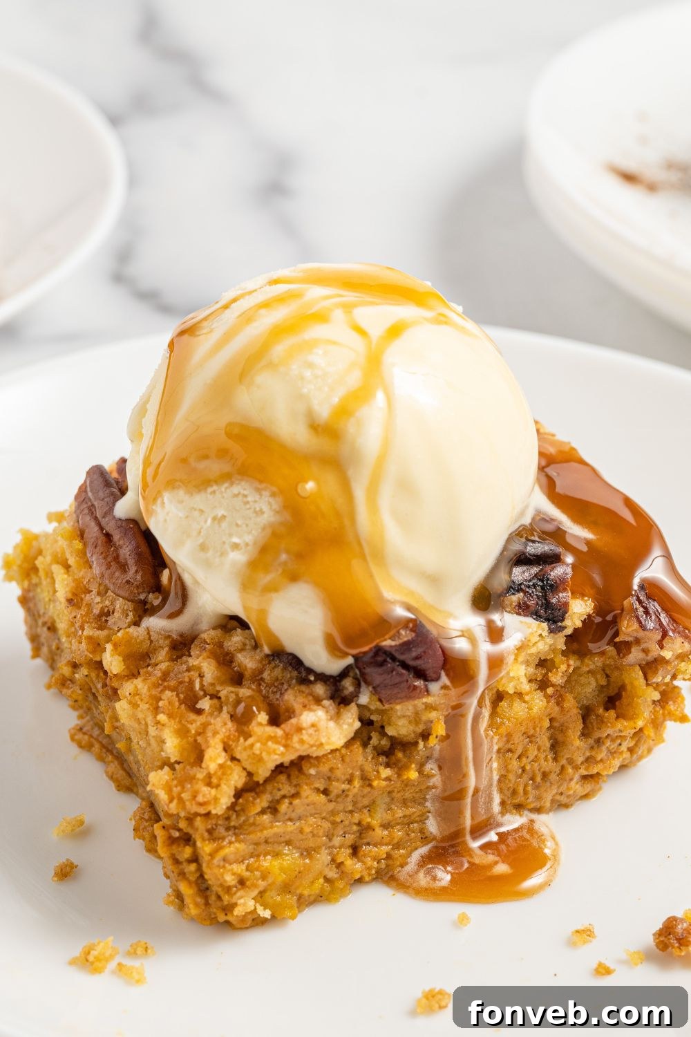 A close-up shot of a slice of Pumpkin Dump Cake on a white plate, served warm with a scoop of vanilla ice cream and a drizzle of caramel sauce.